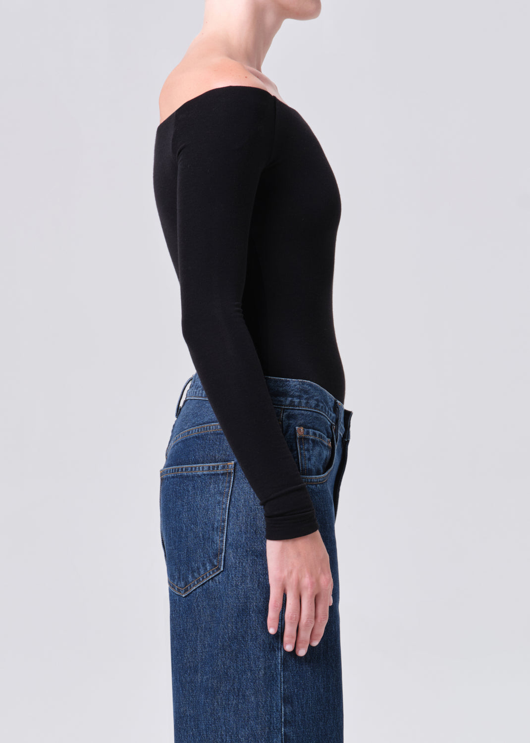 Person wearing a black long-sleeve top and blue jeans on a light gray background