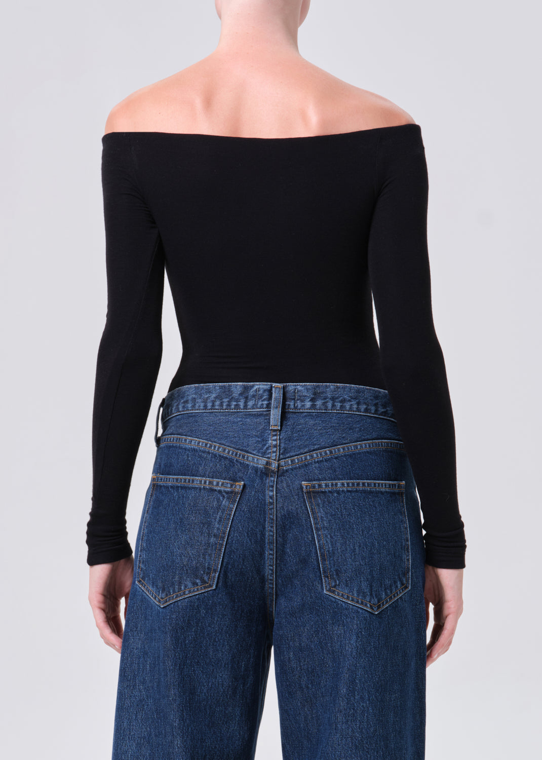 Person wearing a black off-shoulder top and blue jeans on a plain background