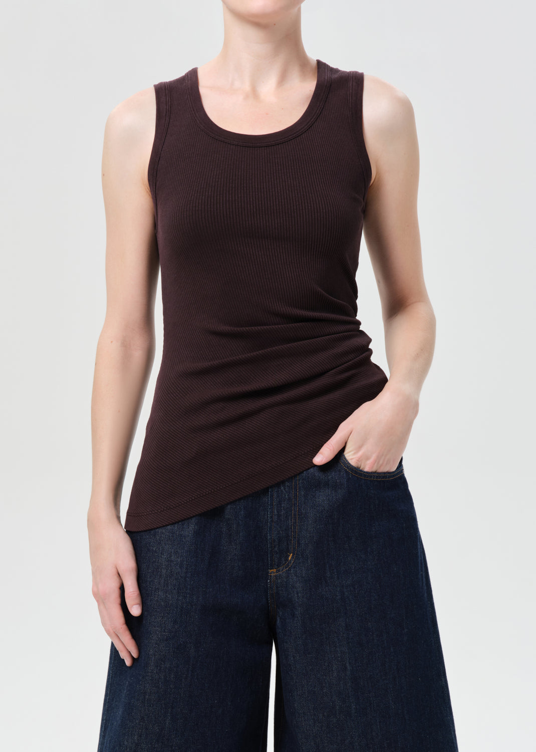 Person wearing a brown tank top and dark blue jeans on a light gray background