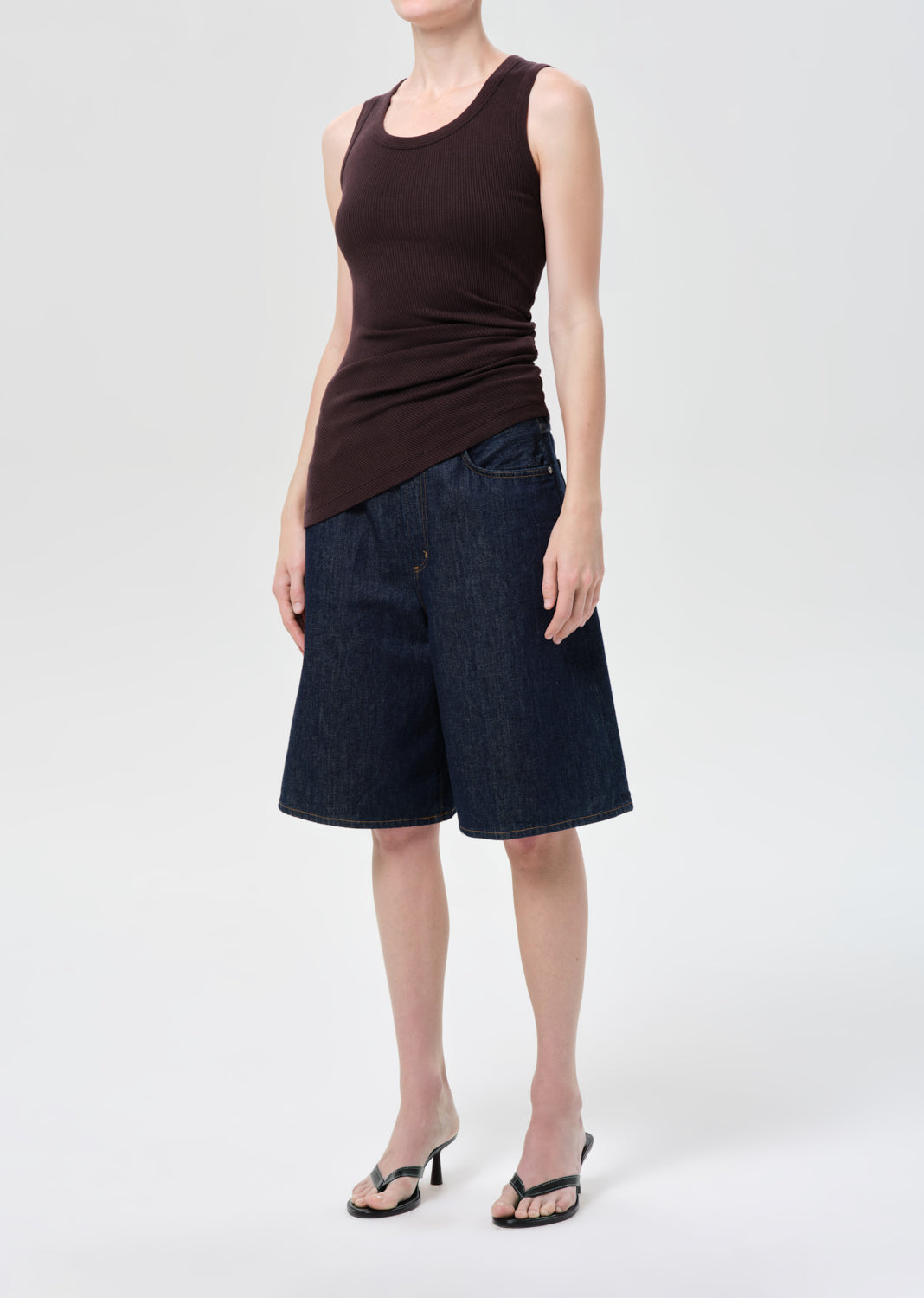 Person wearing a brown tank top and dark denim shorts on a white background