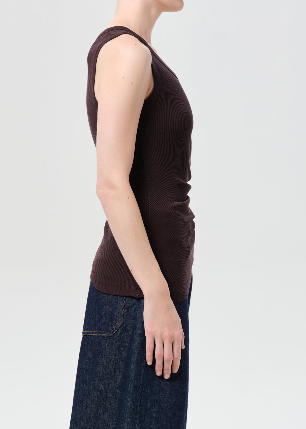 Person wearing a brown sleeveless top and blue jeans on a light gray background