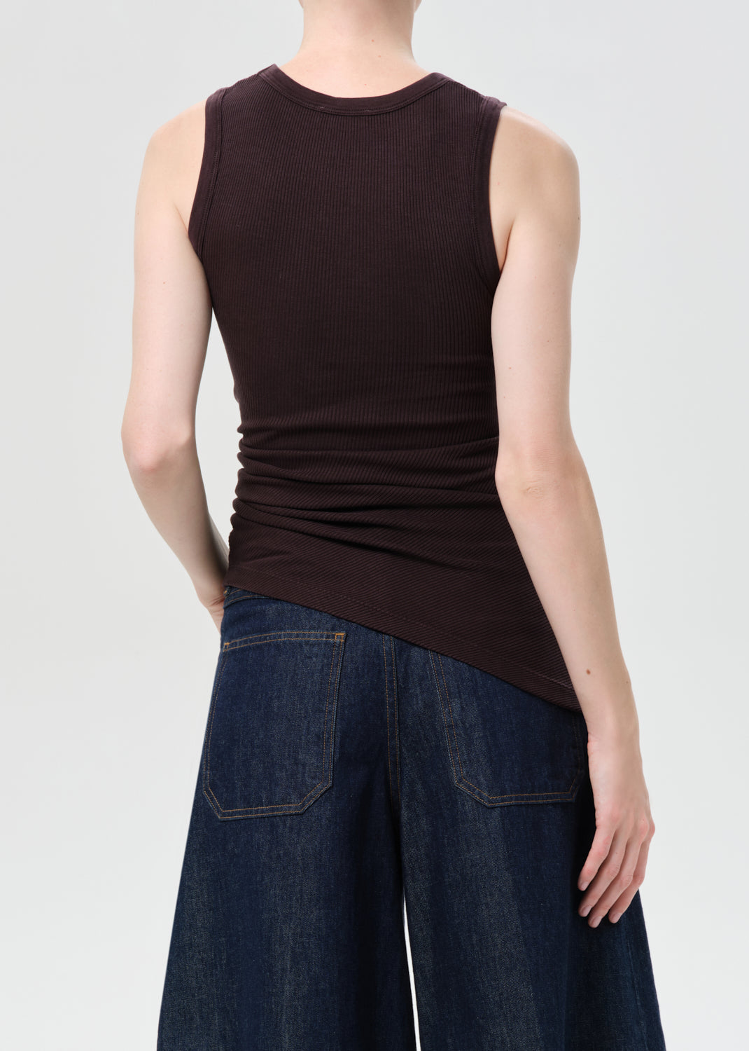 Person wearing a brown sleeveless top and blue jeans on a white background