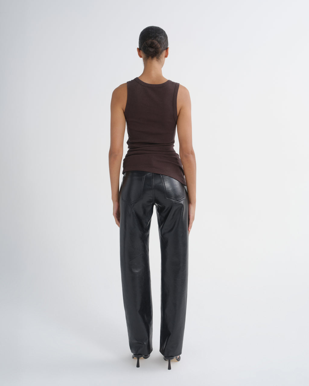 A model shown from the back wearing a dark brown sleeveless top and shiny black wide-leg pants against a light gray studio background.