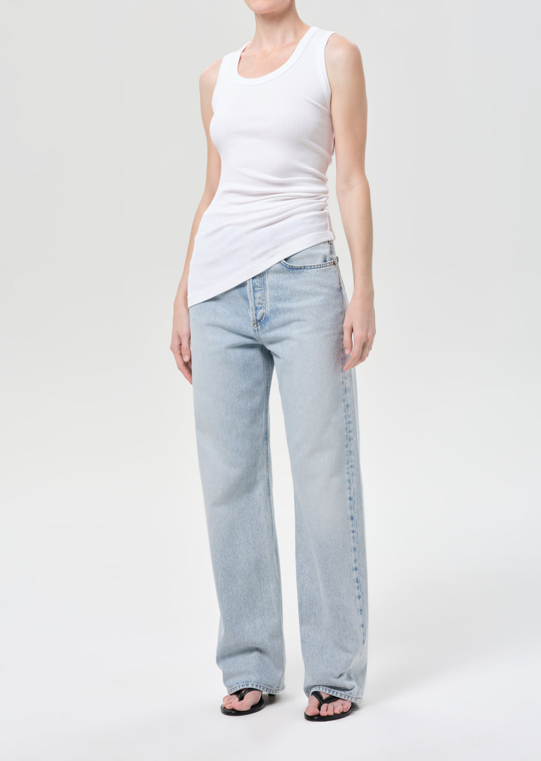 Person wearing a white tank top and light blue jeans on a plain background