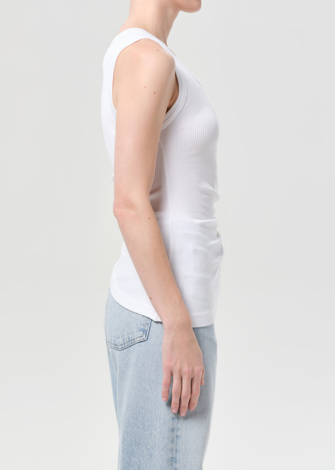 Person wearing a white tank top and light blue jeans on a plain background
