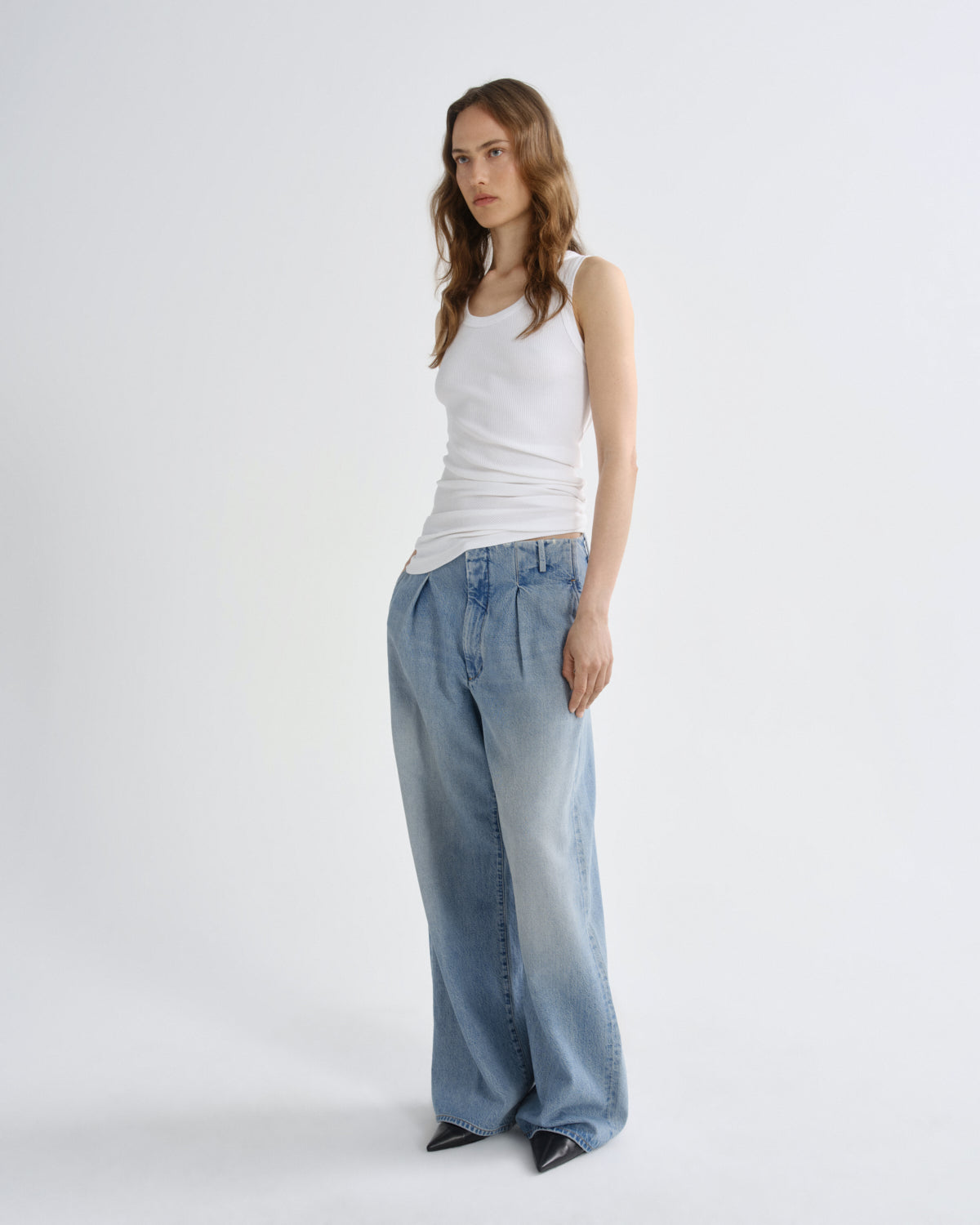 A woman modeling a white ribbed tank top and wide-leg light blue denim jeans against a plain white studio background.