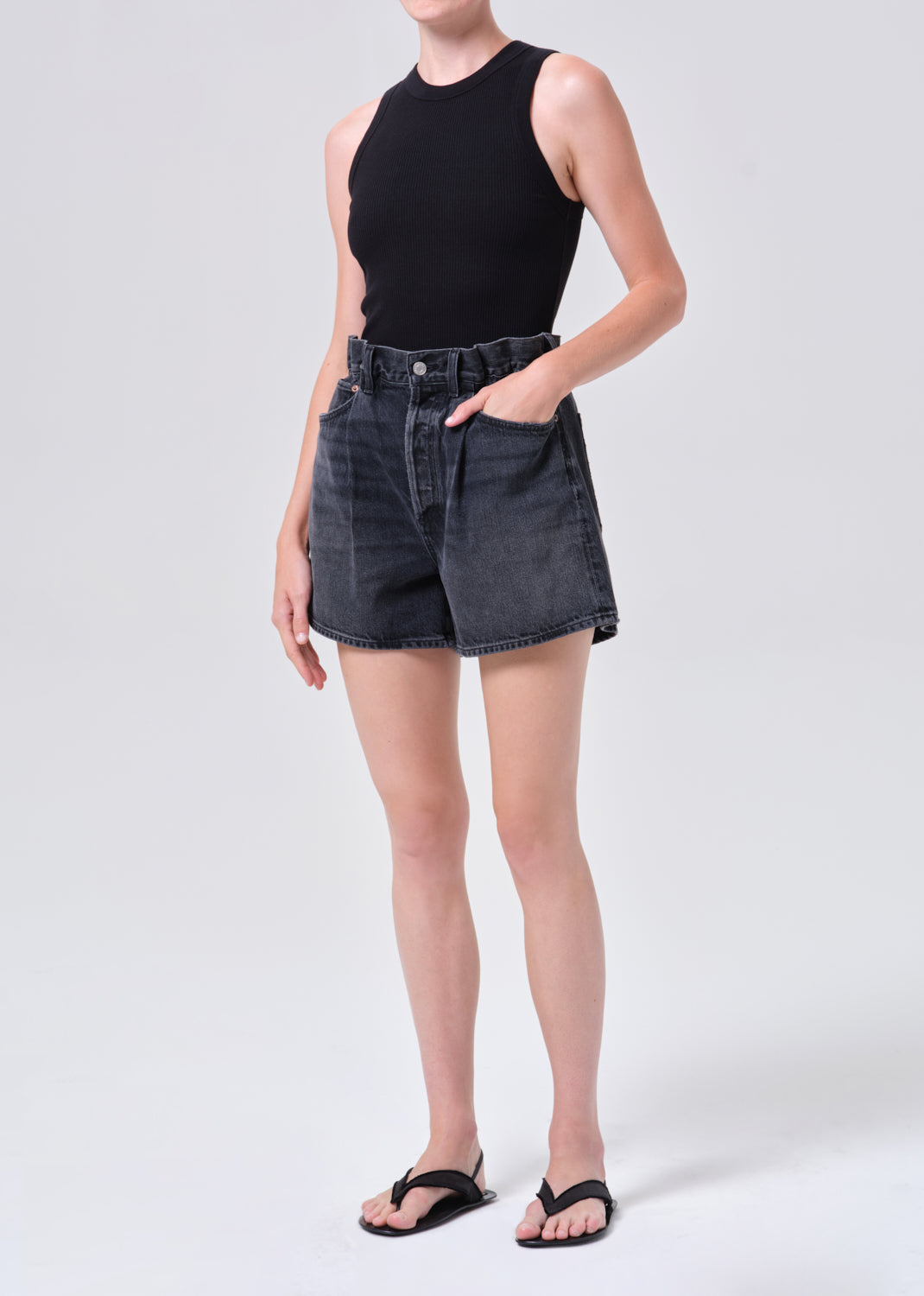 Person wearing black sleeveless top and denim shorts on a white background