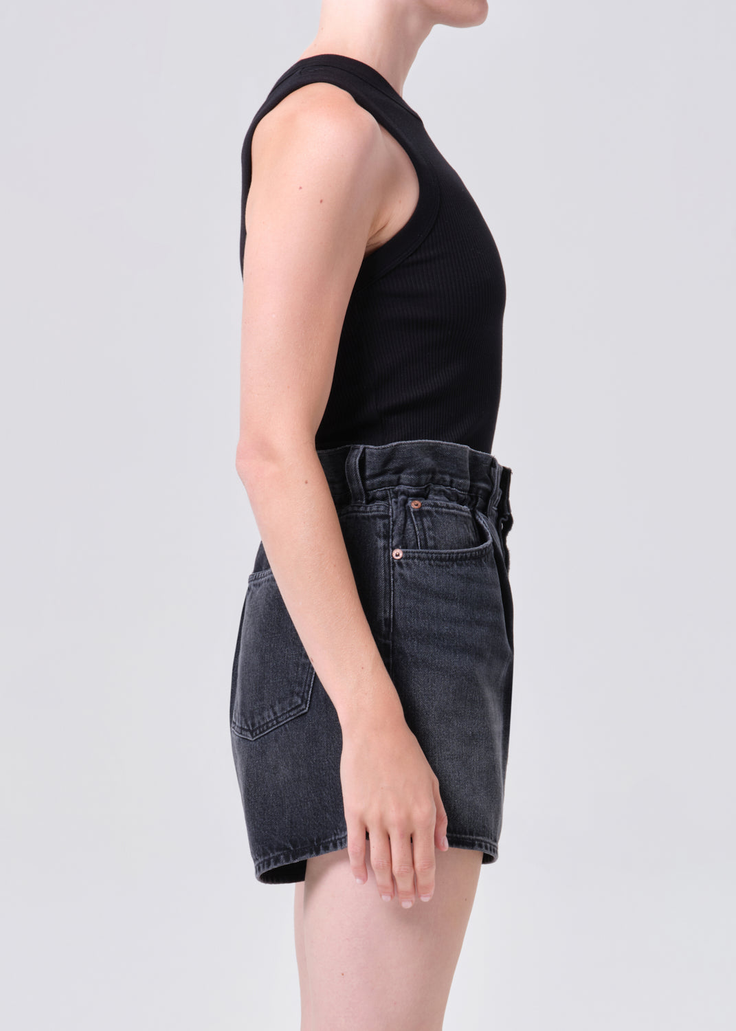 Person wearing a black sleeveless top and dark denim shorts on a white background