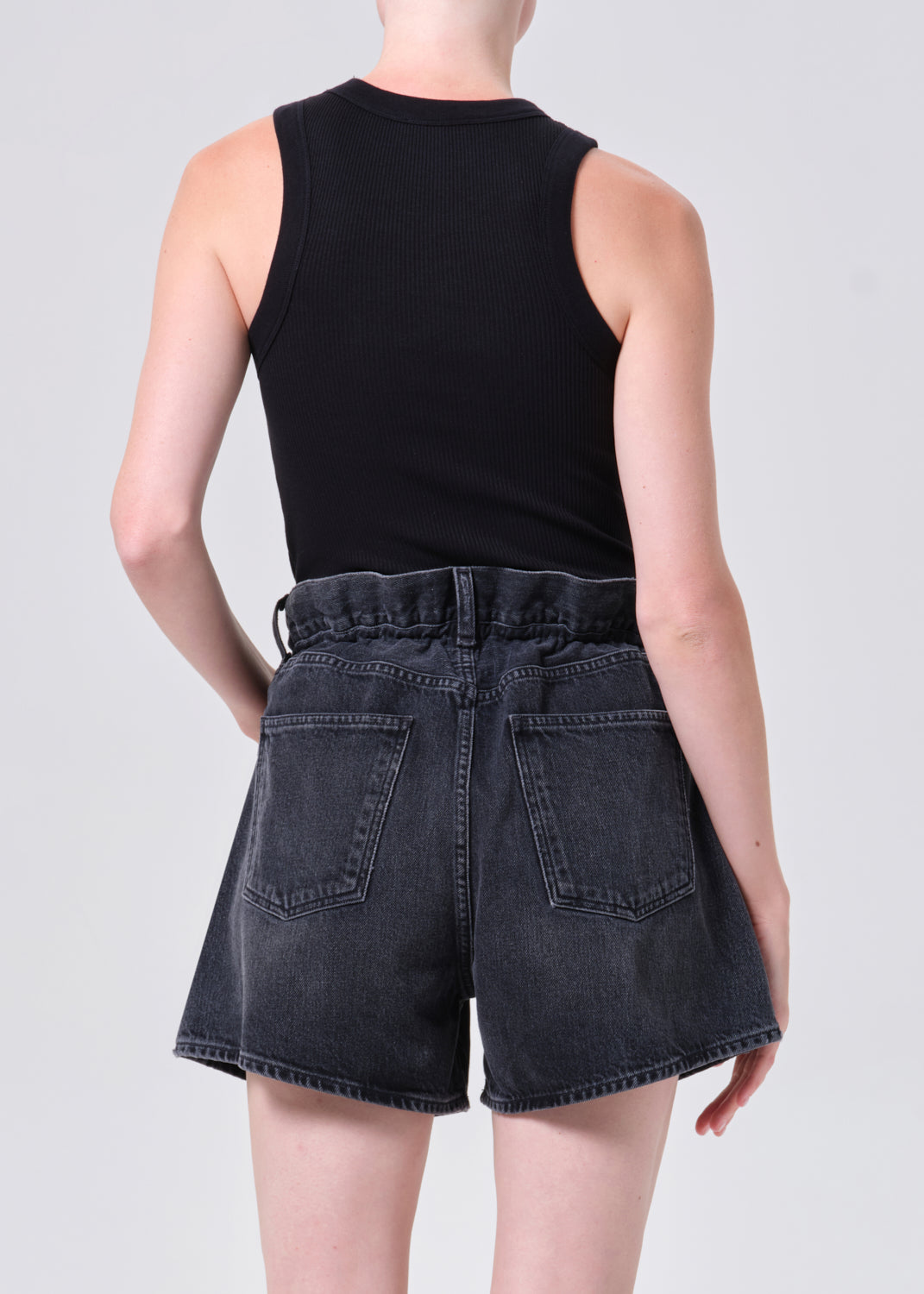 Person wearing black tank top and denim shorts on a plain background