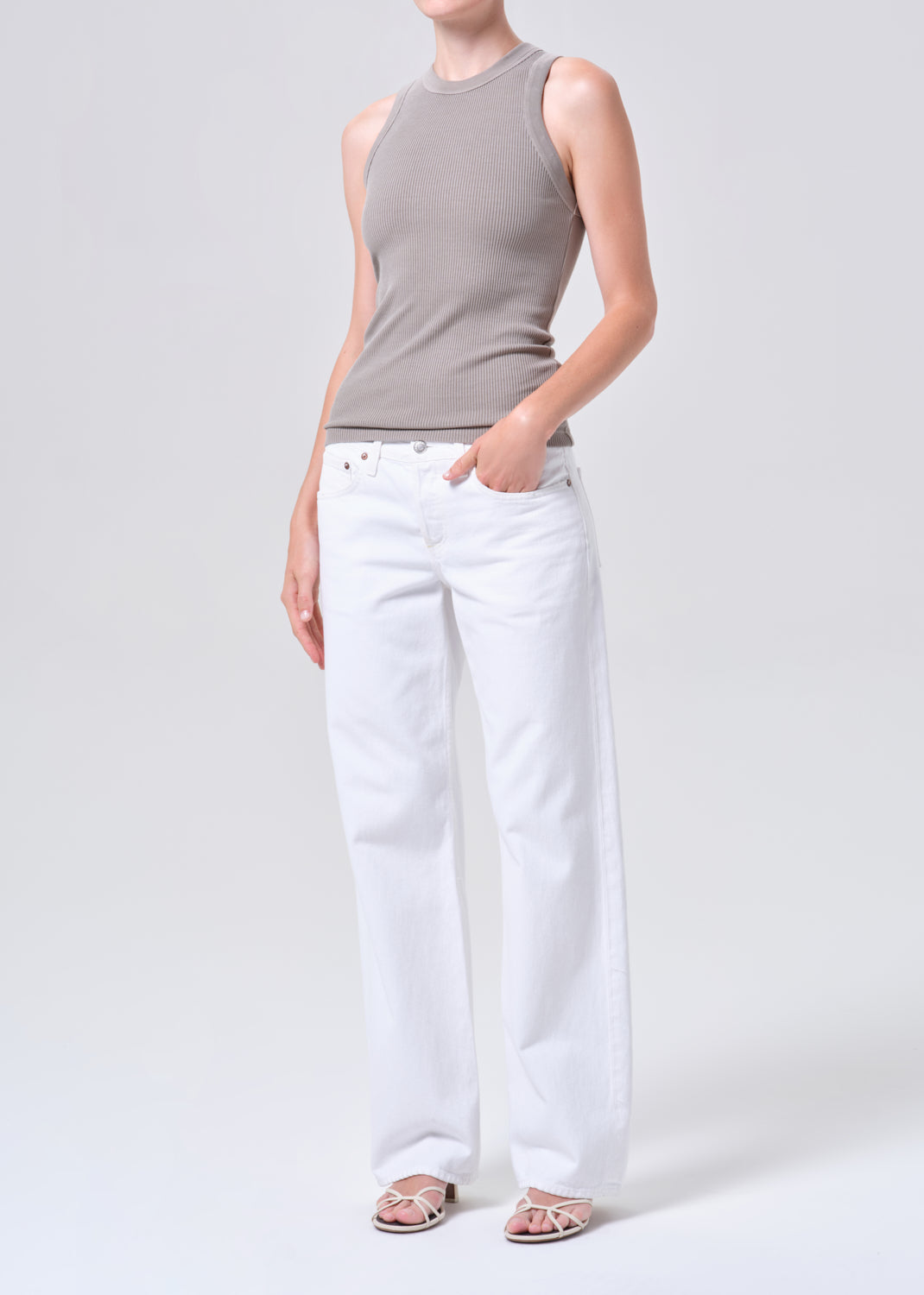 Person wearing a gray sleeveless top and white pants on a plain background