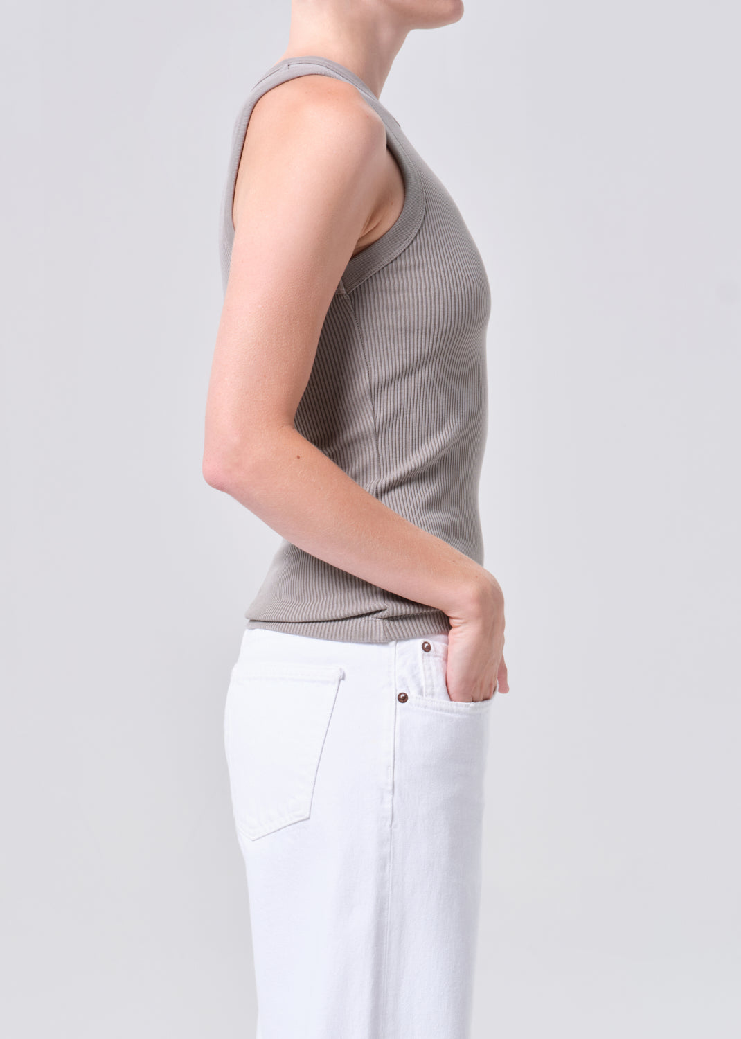 Person wearing a gray ribbed tank top and white pants on a light gray background