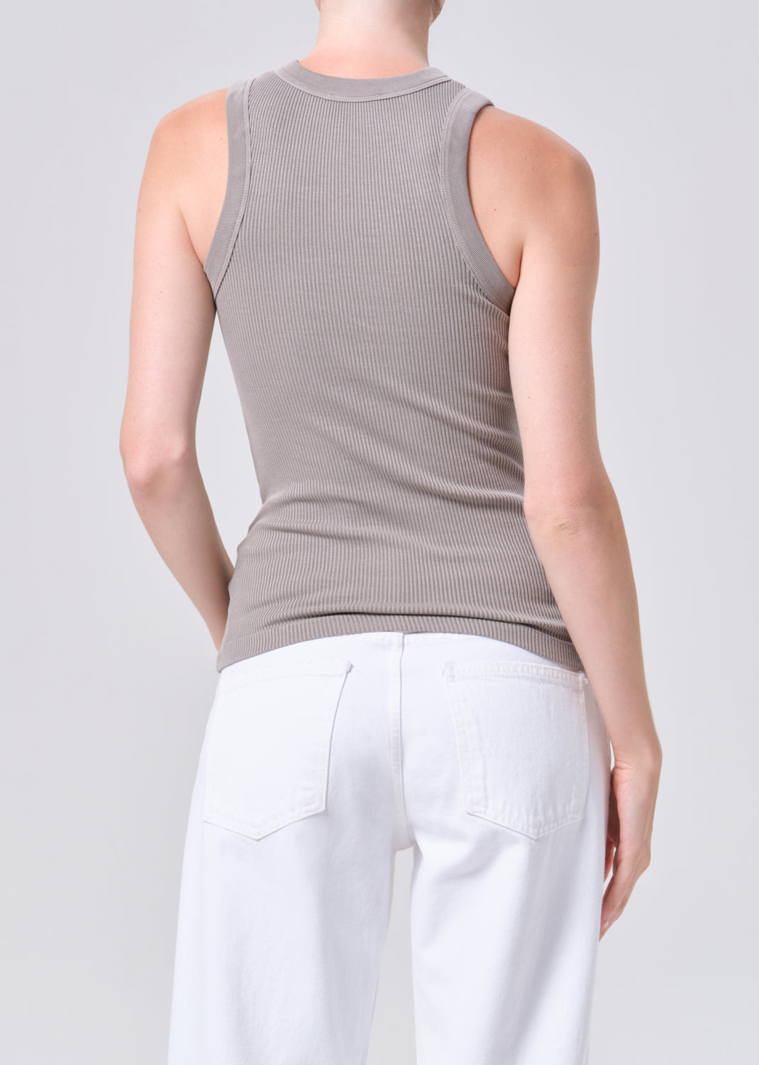 Person wearing a sleeveless ribbed top and white pants on a plain background