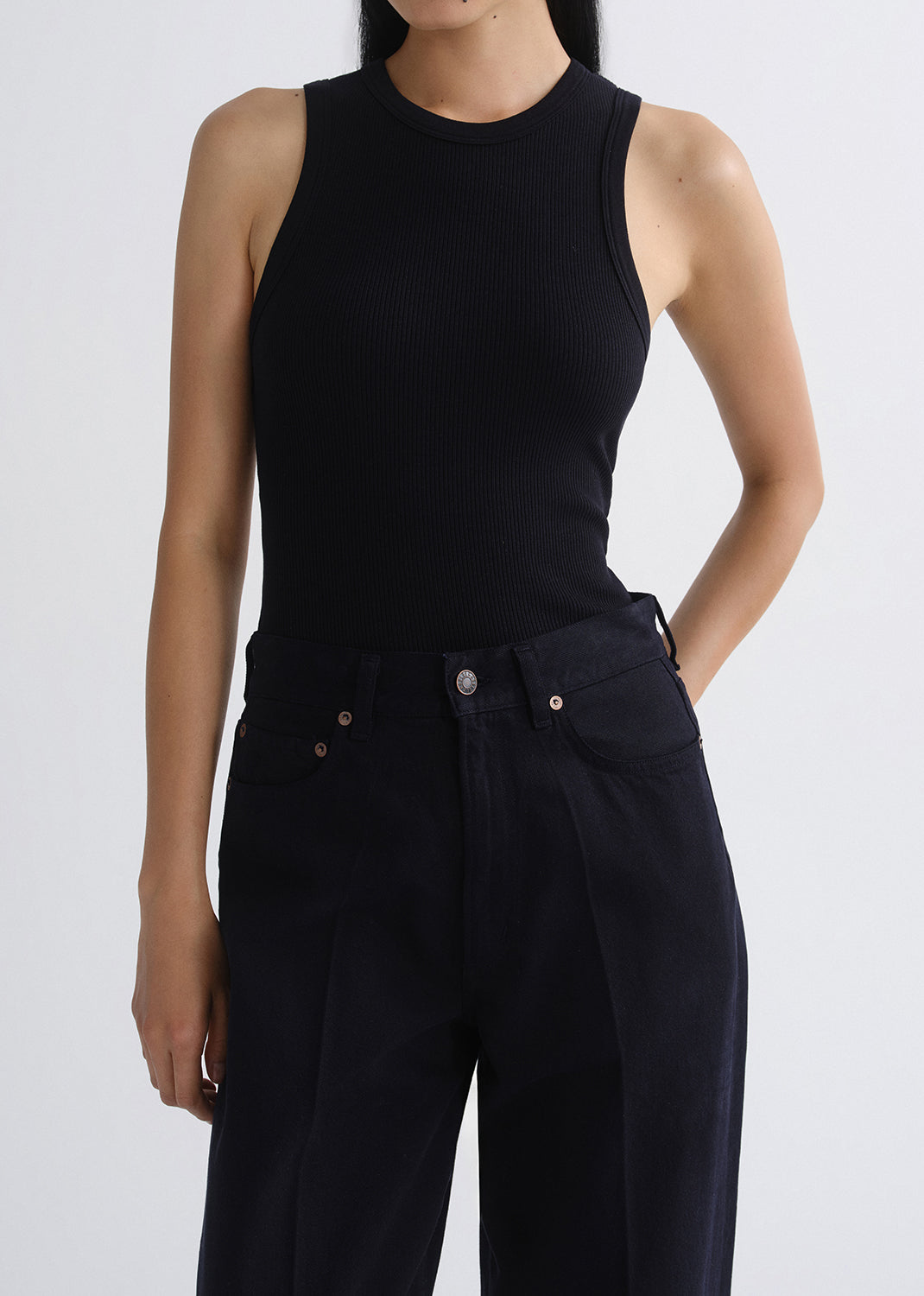Person wearing a black sleeveless top and black pants on a grey background