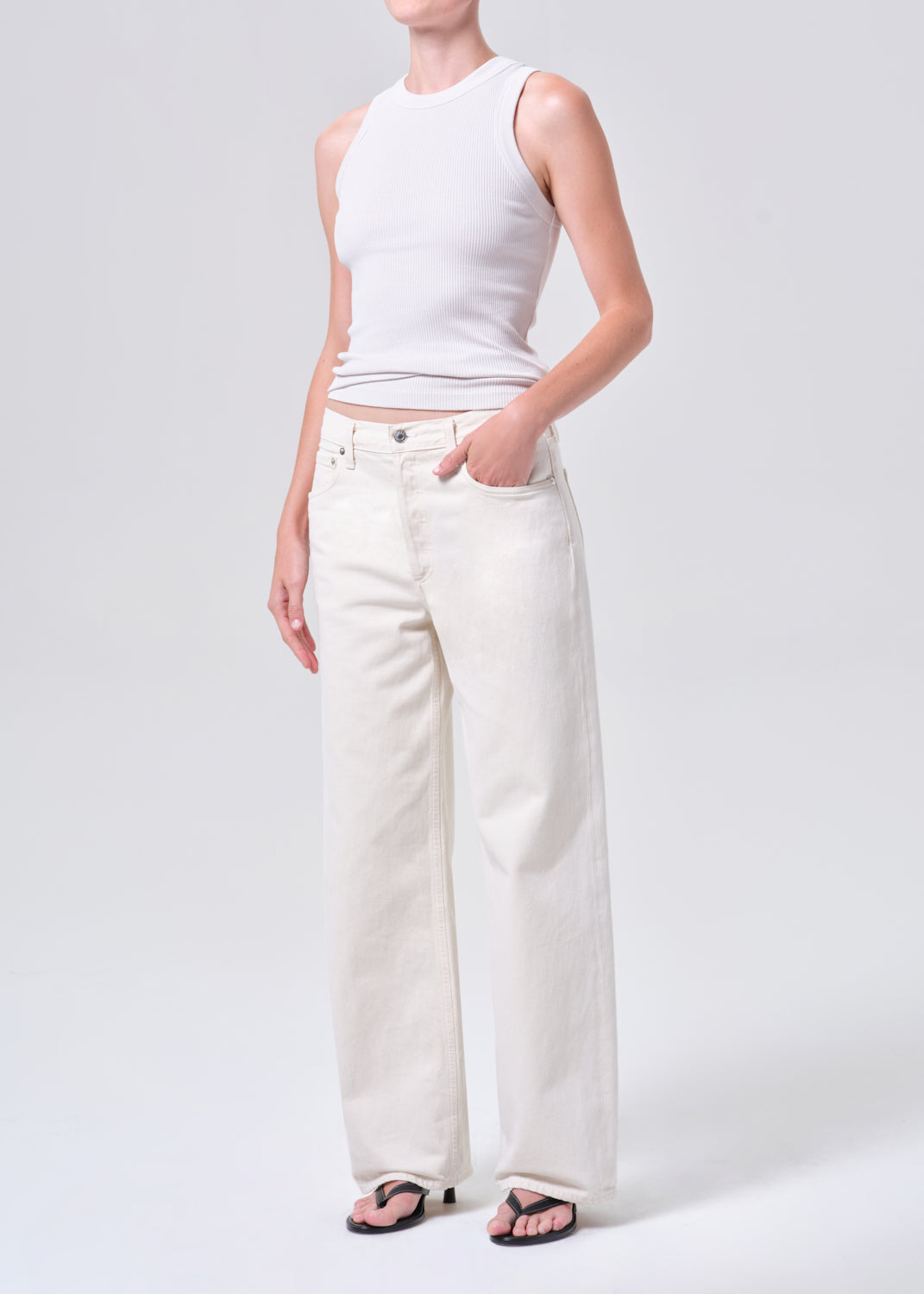 Person wearing a white sleeveless top and light-colored pants on a plain background