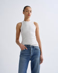 Person wearing a white sleeveless top and blue jeans on a light gray background