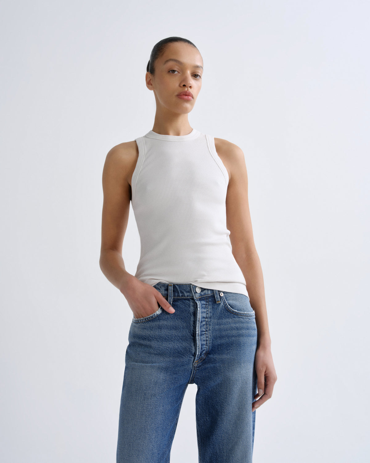 Person wearing a white sleeveless top and blue jeans on a light gray background