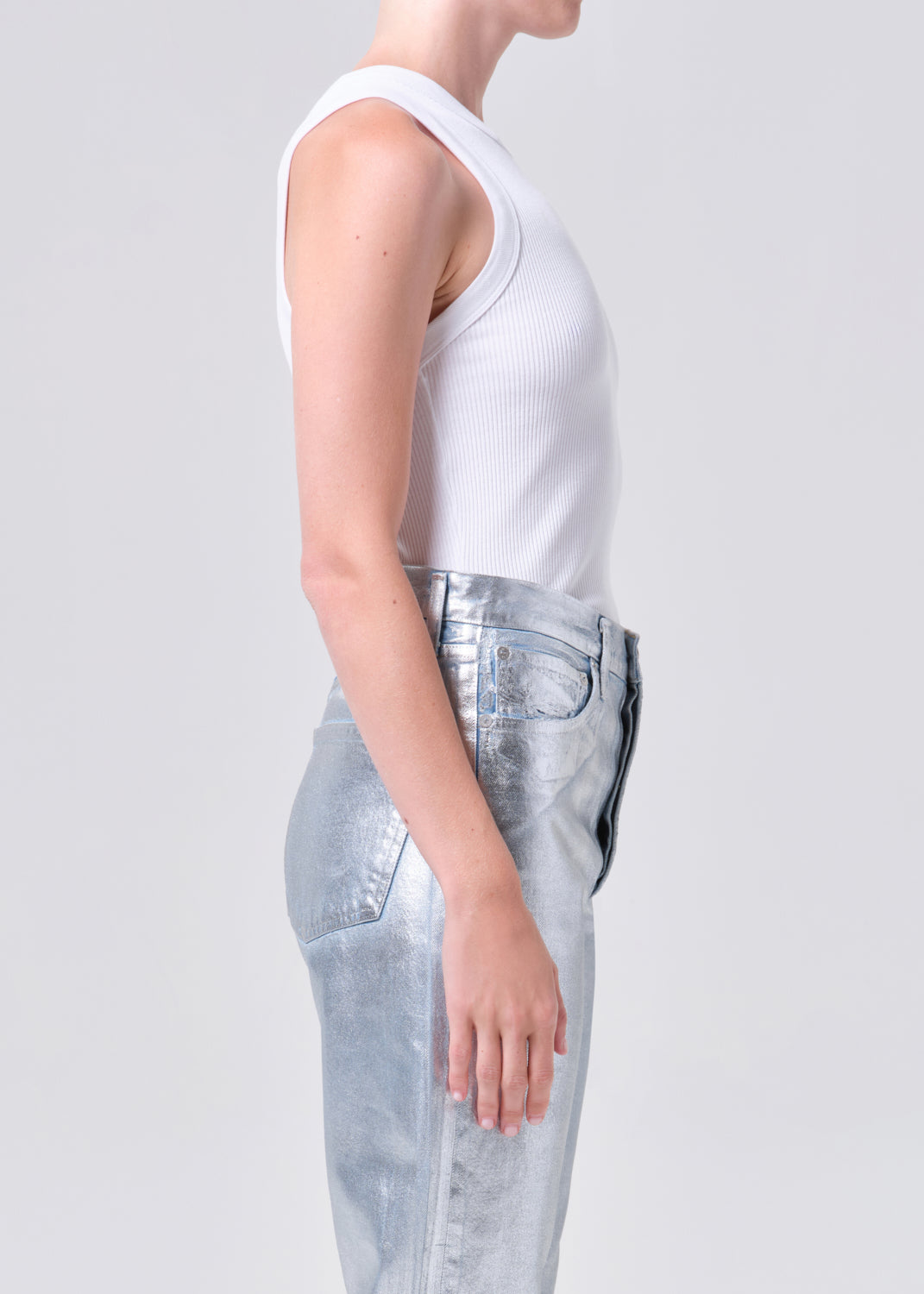 Person wearing a white sleeveless top and light blue jeans on a plain background