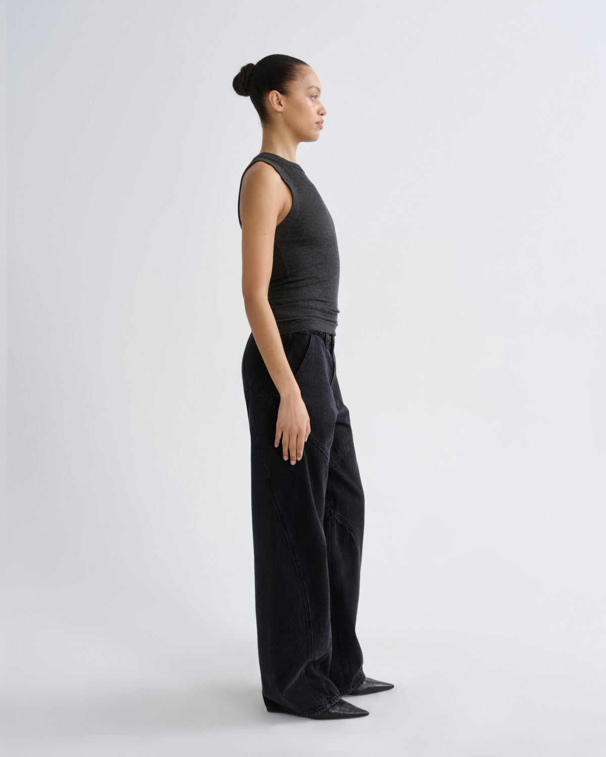 A model in side profile wearing a dark charcoal gray sleeveless top and matching dark charcoal wide-leg pants, standing against a light gray studio background.