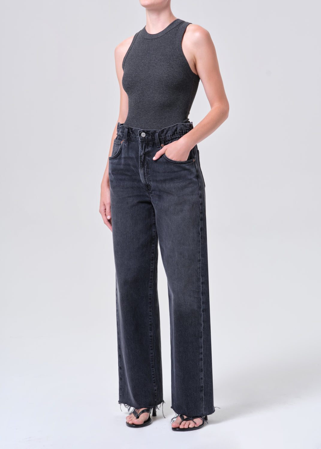 Person wearing a dark gray sleeveless top and high-waisted jeans on a white background