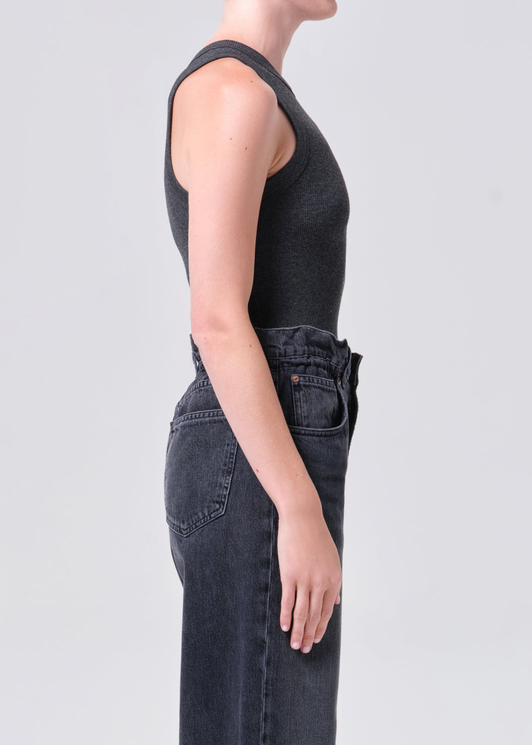 Person wearing a black sleeveless top and dark jeans on a light gray background