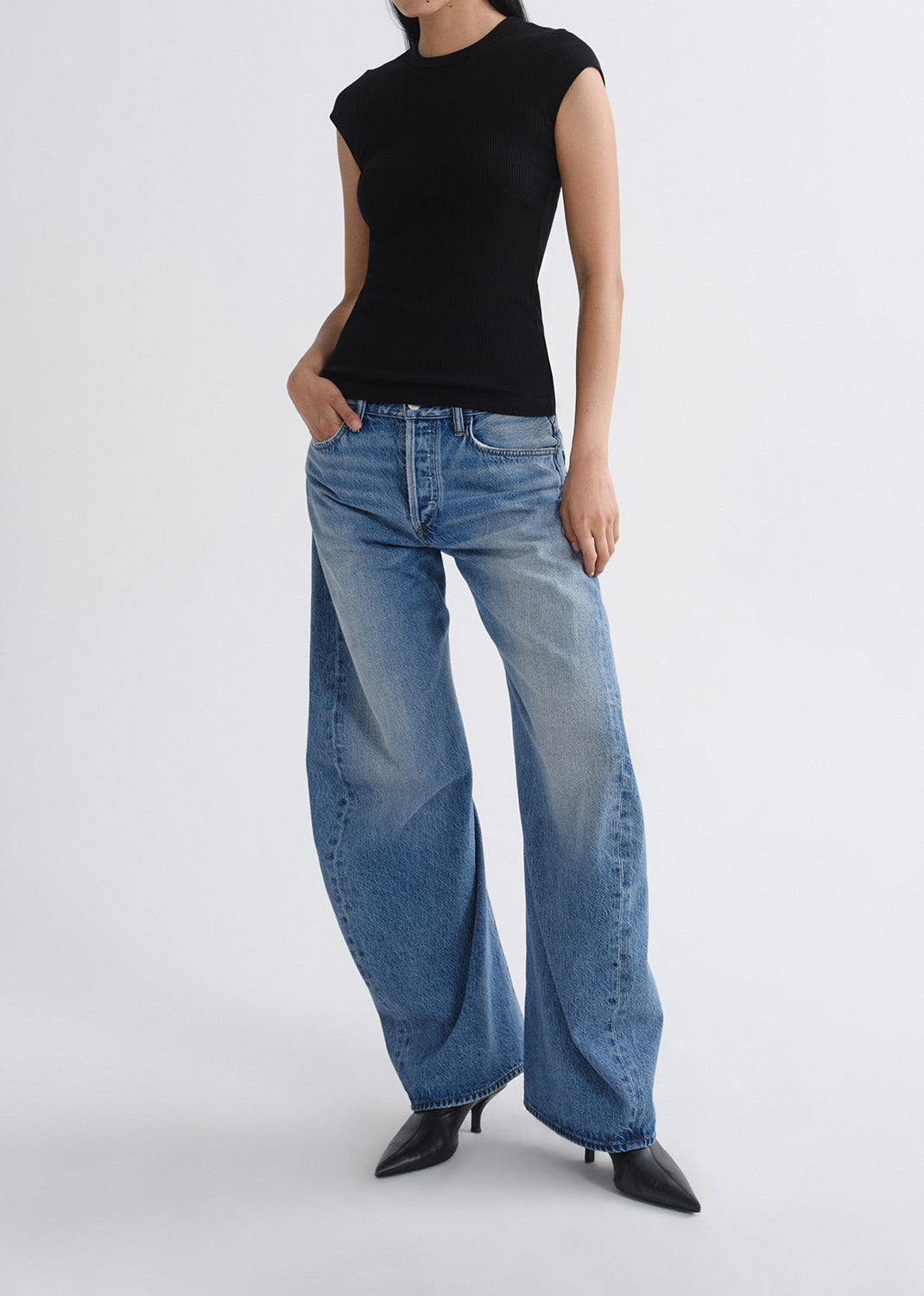 Person wearing a black sleeveless top and blue jeans on a grey background