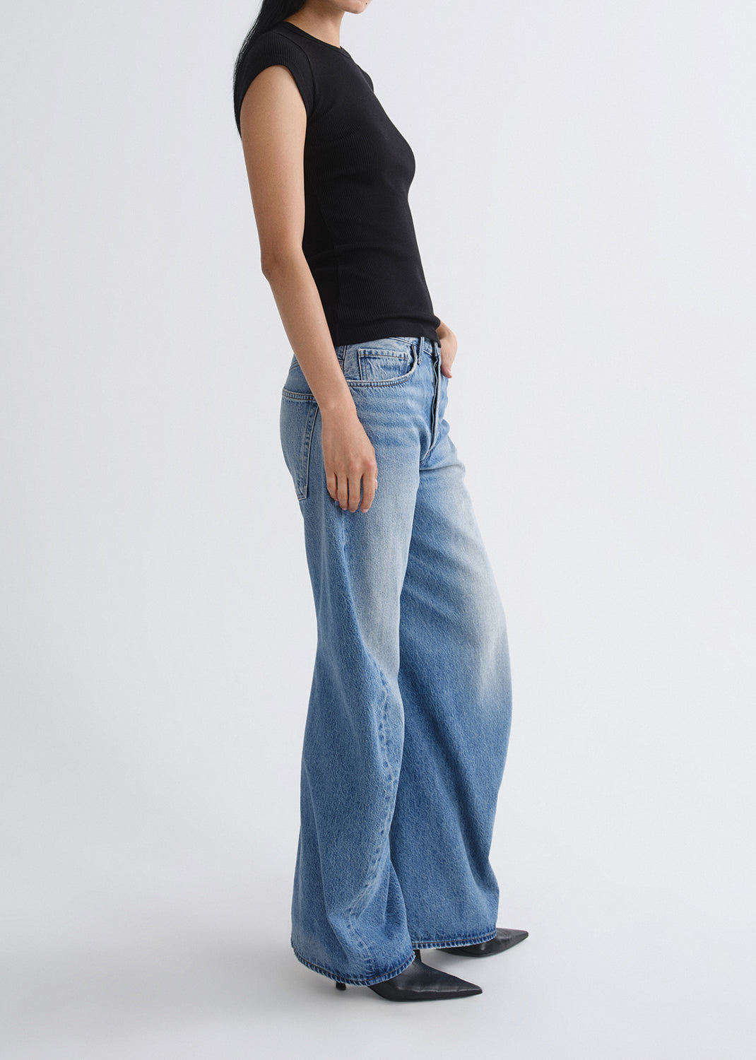 Person wearing a black top and blue jeans on a grey background