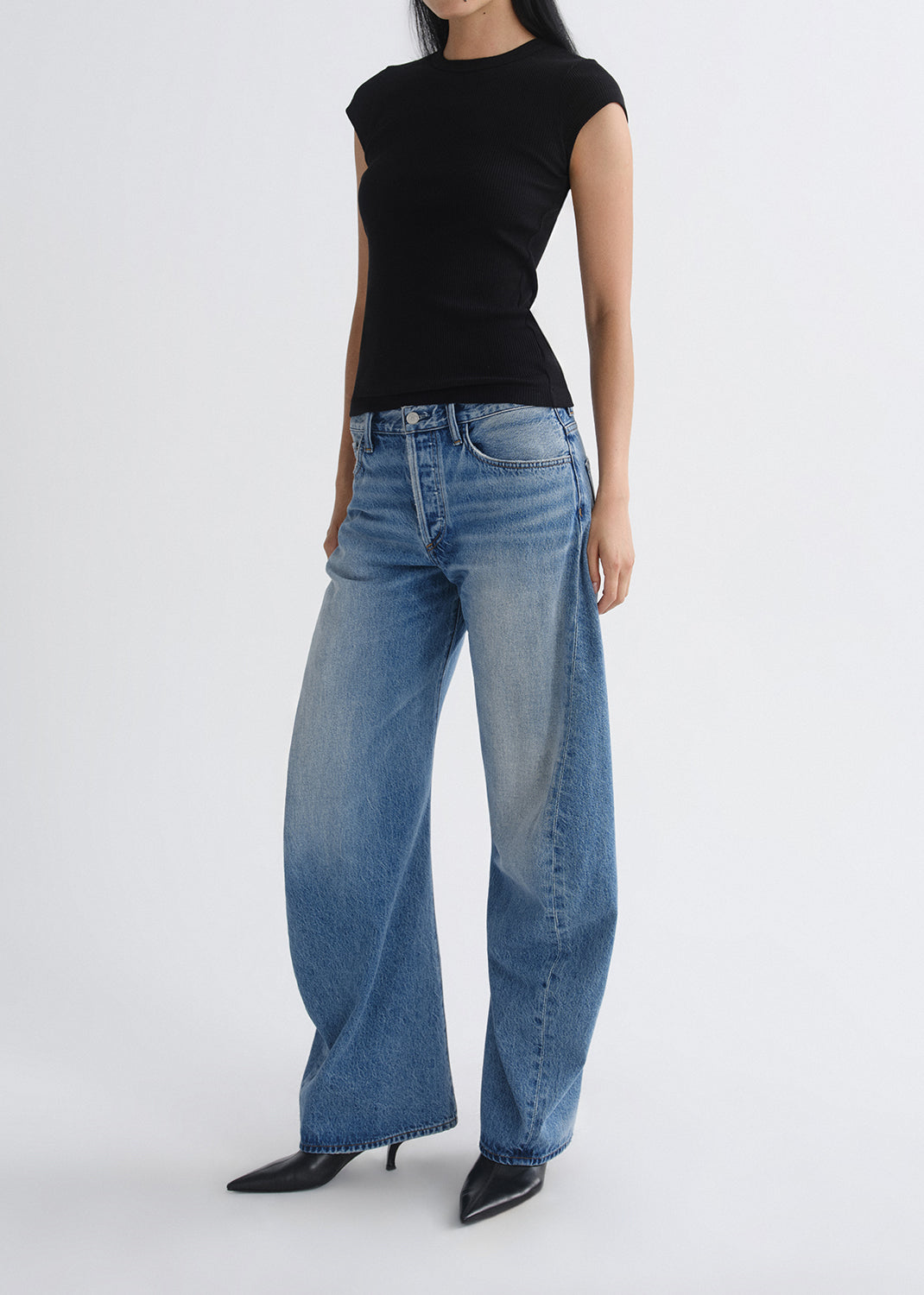 Person wearing a black top and blue jeans on a grey background