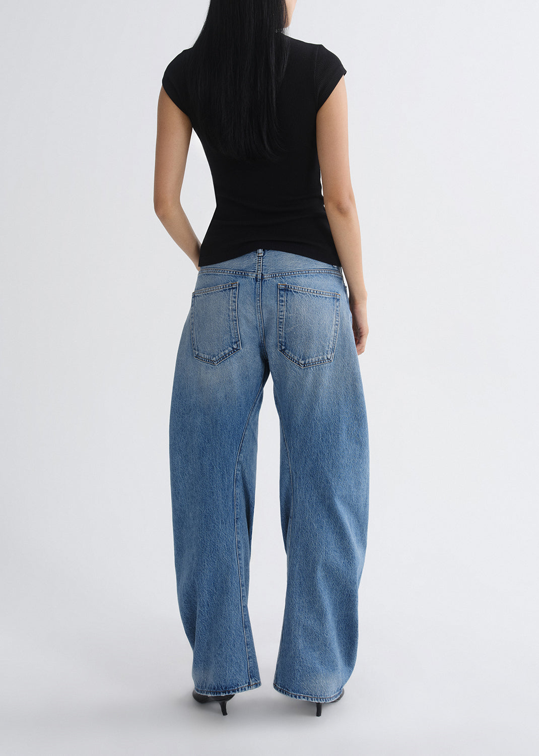 Person wearing blue jeans and a black top on a grey background