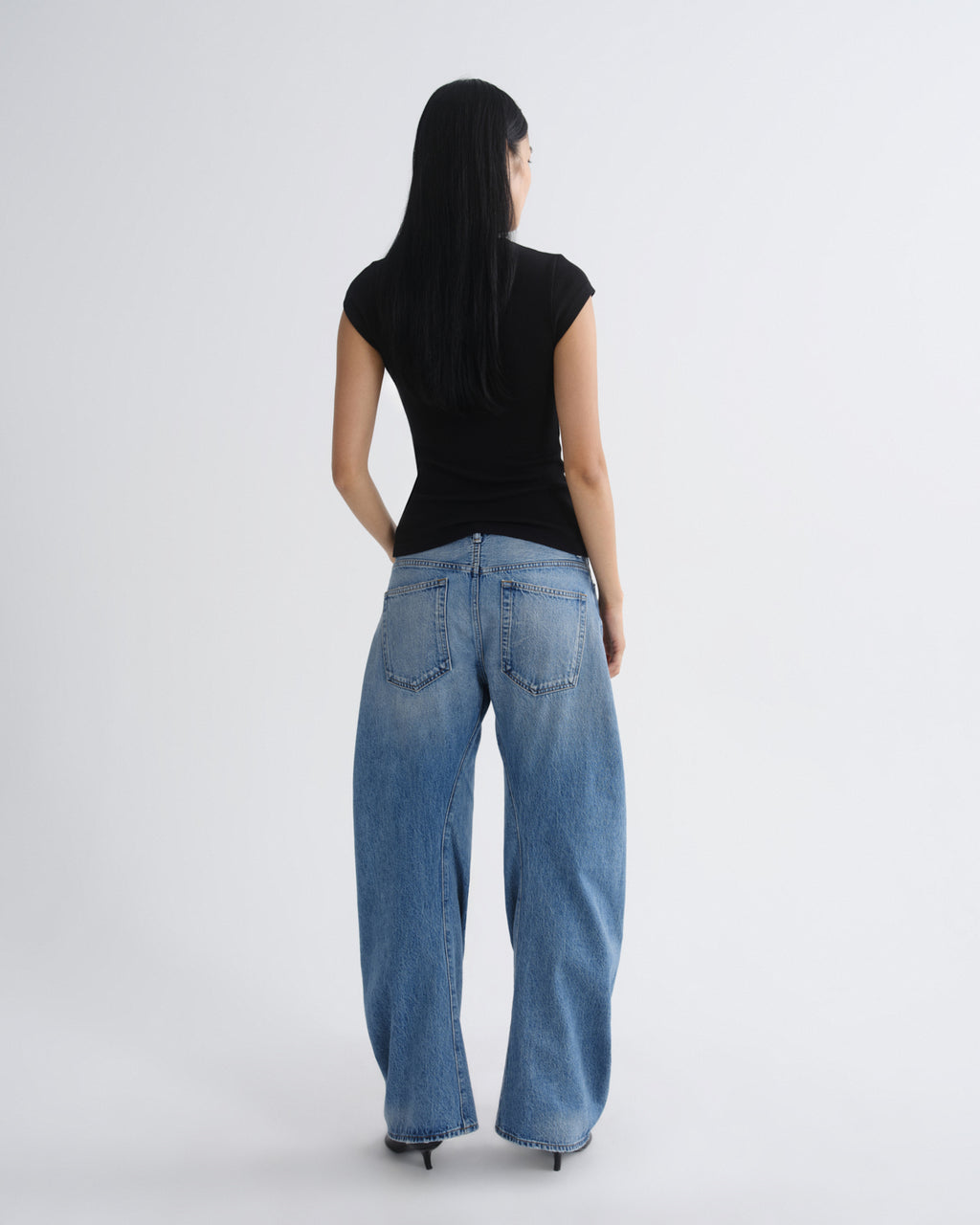 Person wearing blue jeans and a black top on a white background