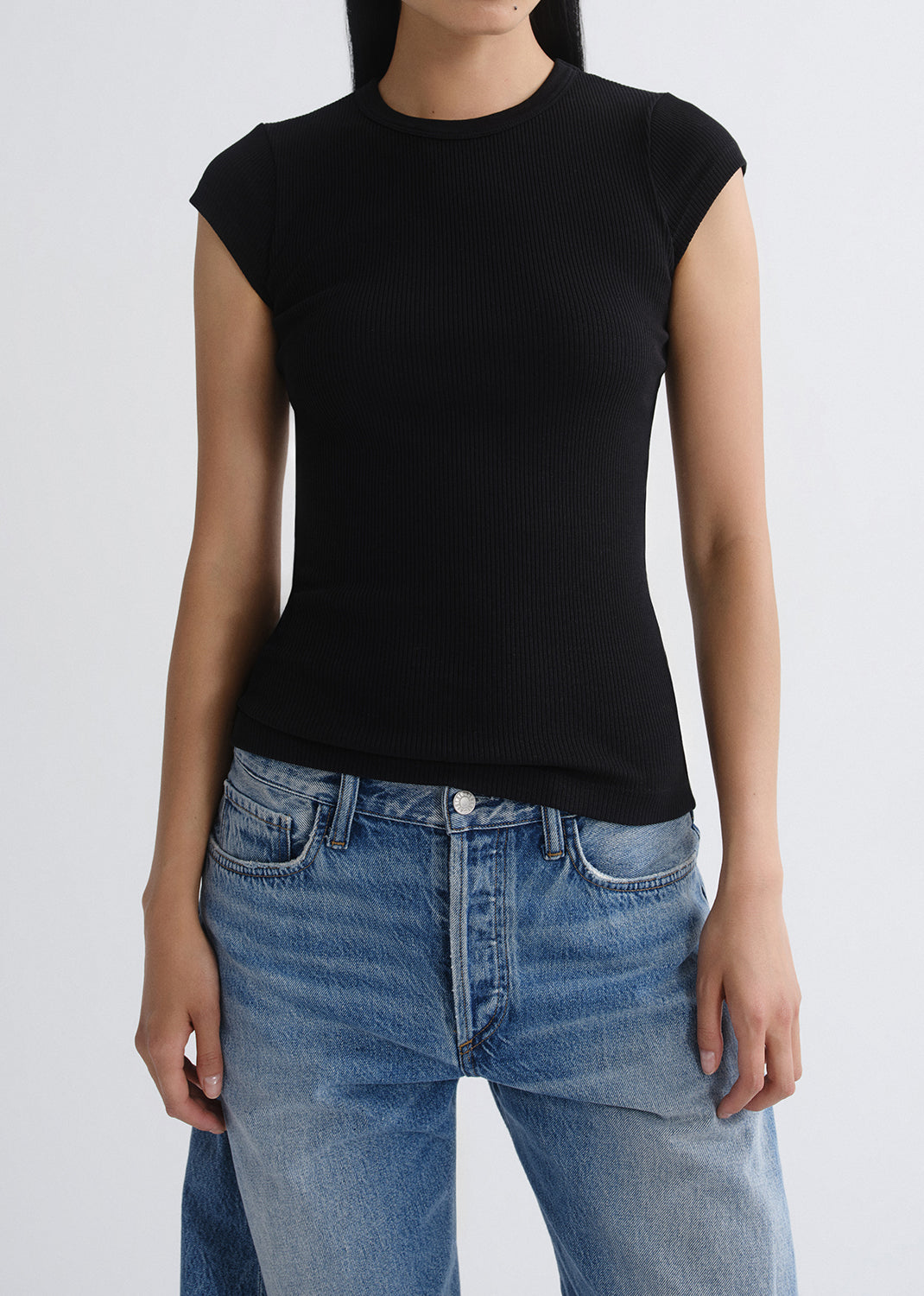 Person wearing a black t-shirt and blue jeans on a grey background
