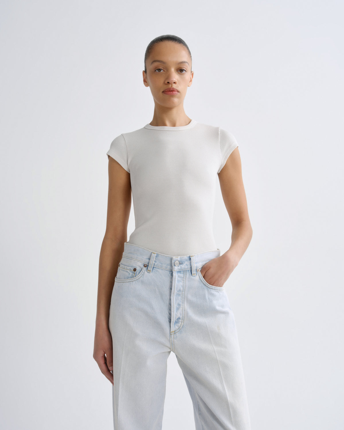 Person wearing a white top and light blue jeans on a plain background