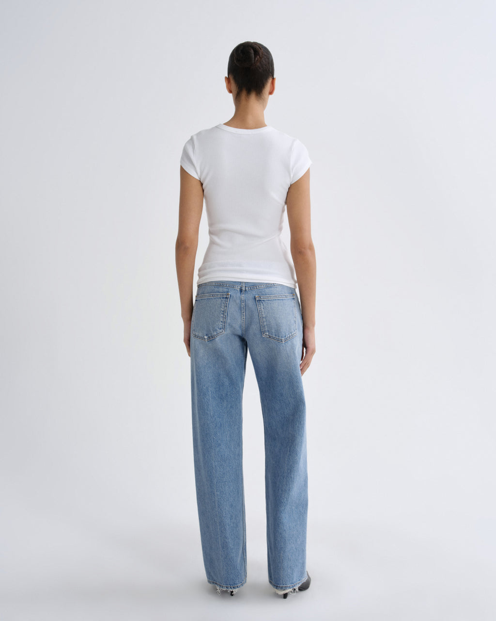 A model shown from the back wearing a white short-sleeve t-shirt and light blue wide-leg jeans against a plain light gray studio background.