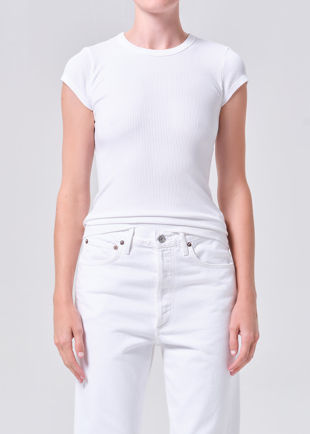 Person wearing a white t-shirt and white jeans on a light gray background