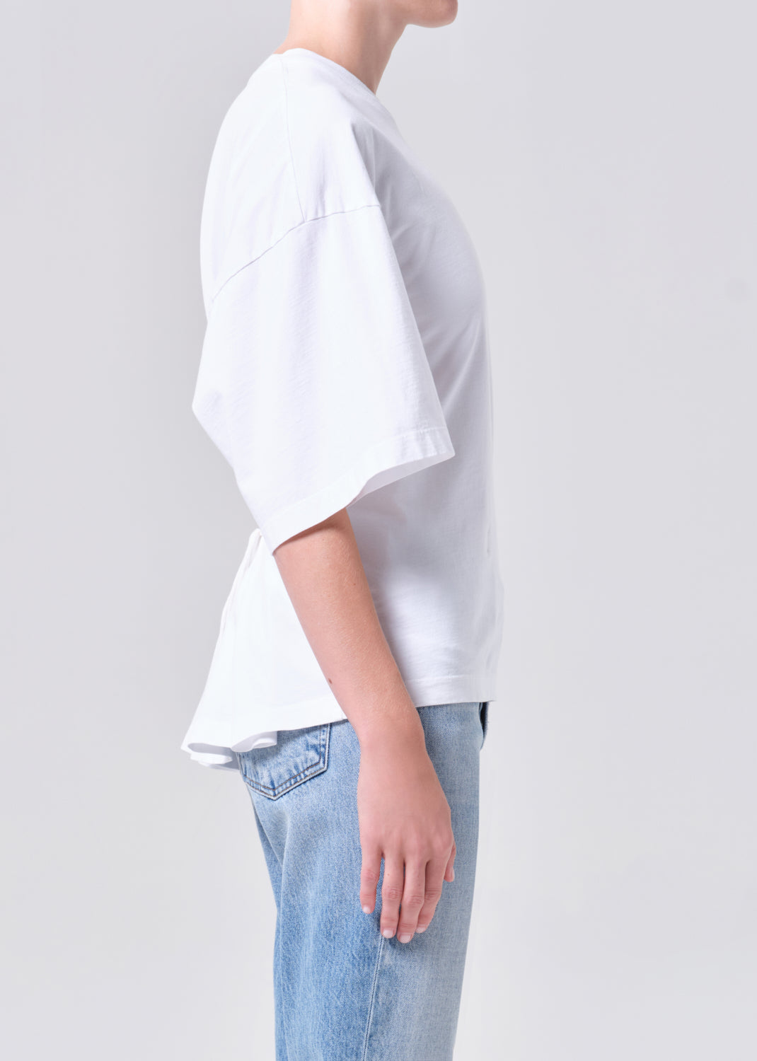 Person wearing a white oversized t-shirt and light blue jeans on a plain background