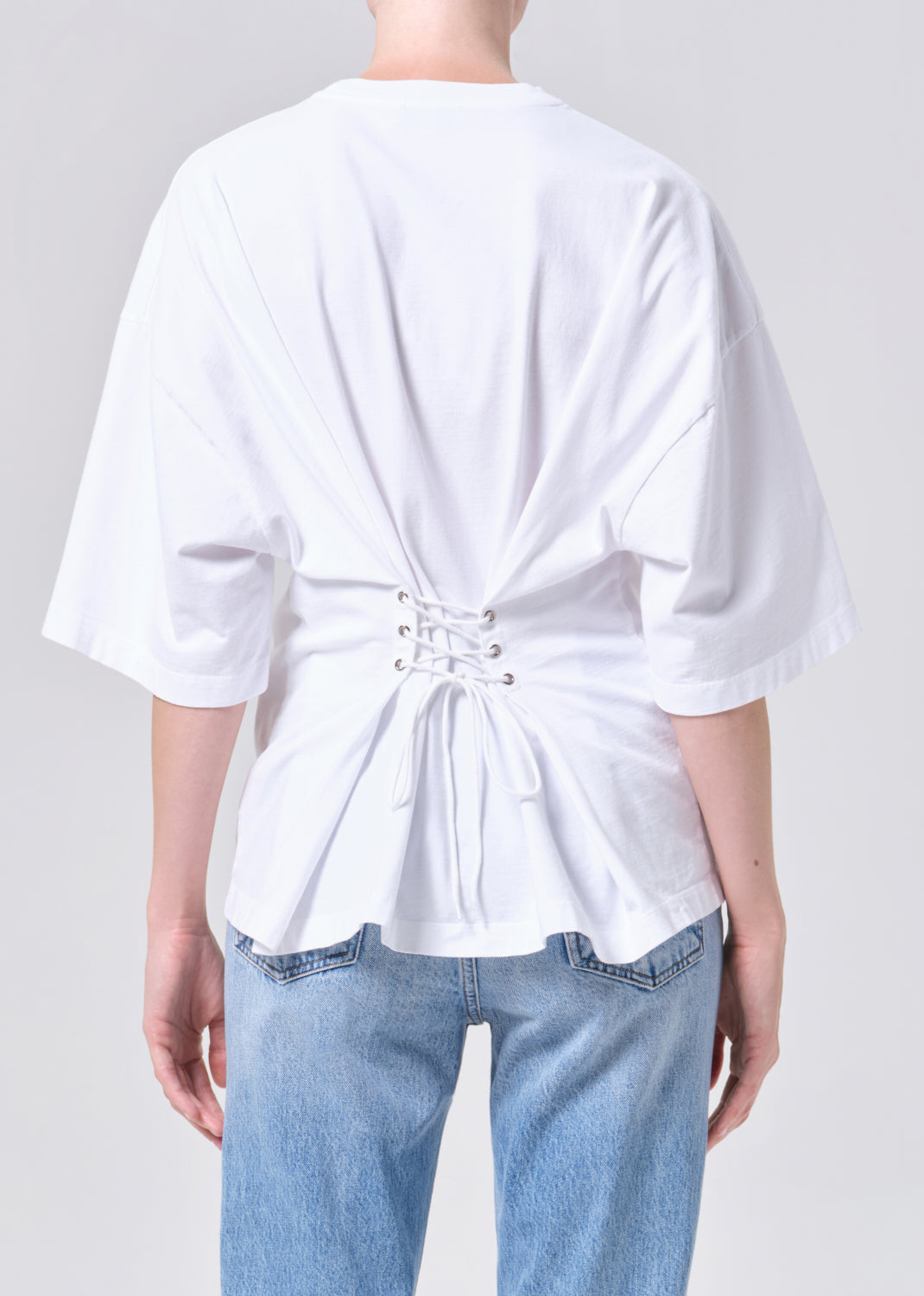 White blouse with a knot detail at the back worn by a person on a plain background