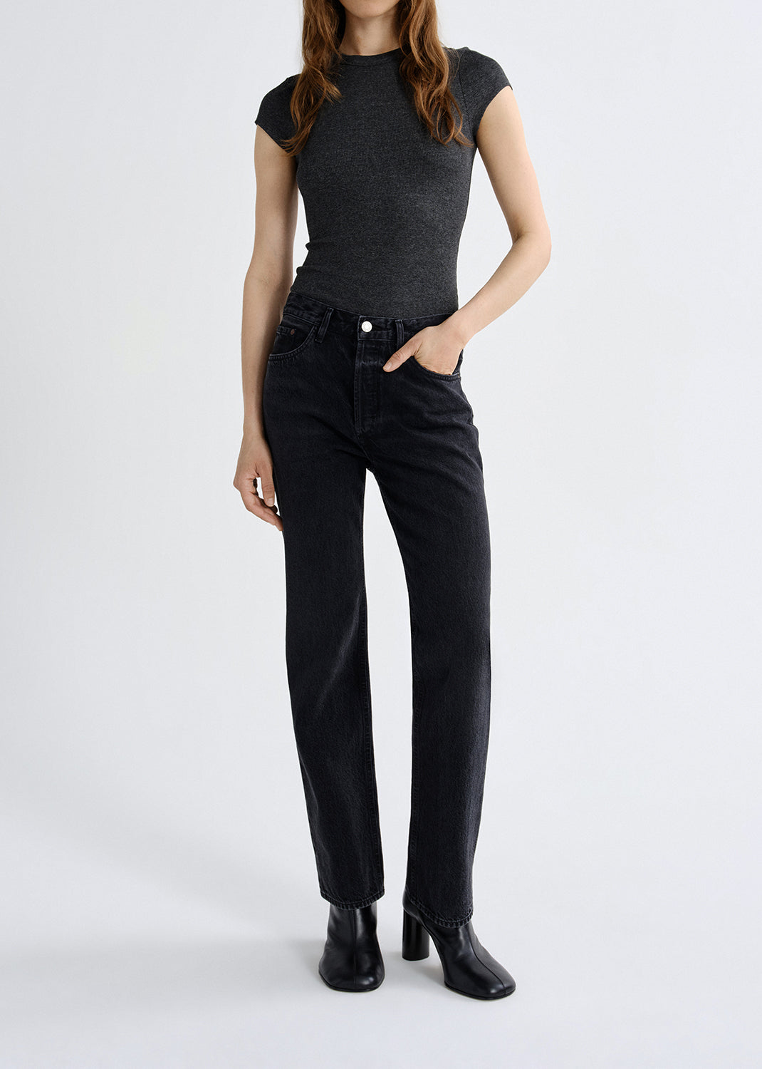 Person wearing a dark gray top and black jeans on a white background
