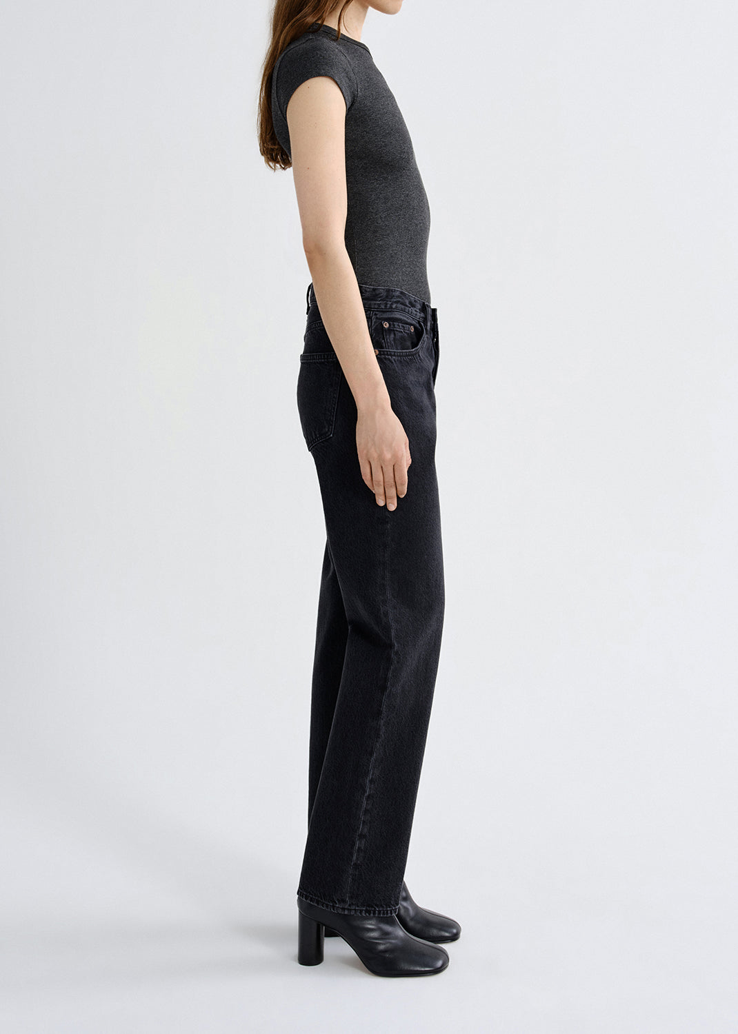 Person wearing a dark gray sleeveless top and black jeans on a white background