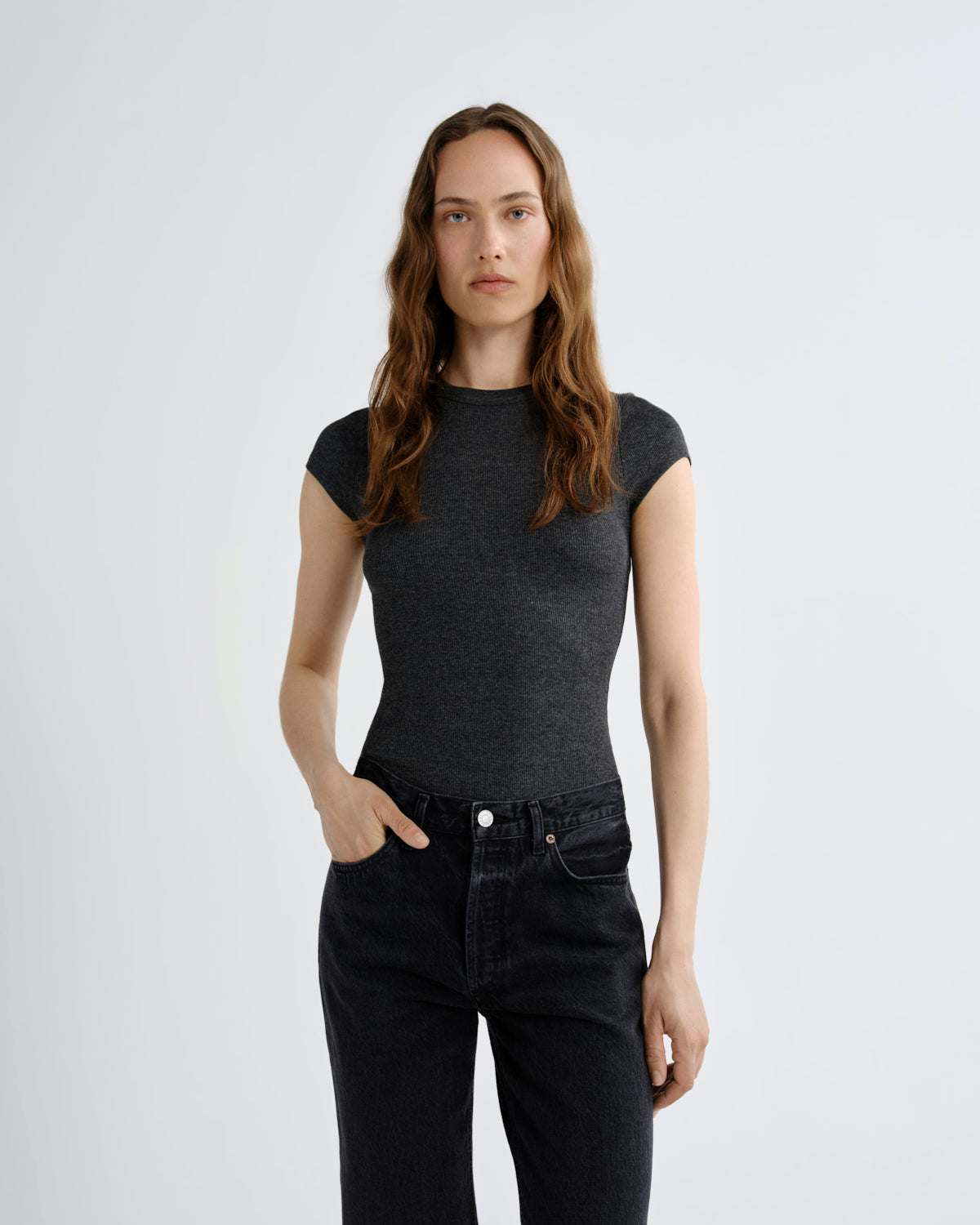 A woman modeling a dark gray heathered short-sleeve crewneck top paired with dark wash jeans, standing against a light gray studio background.