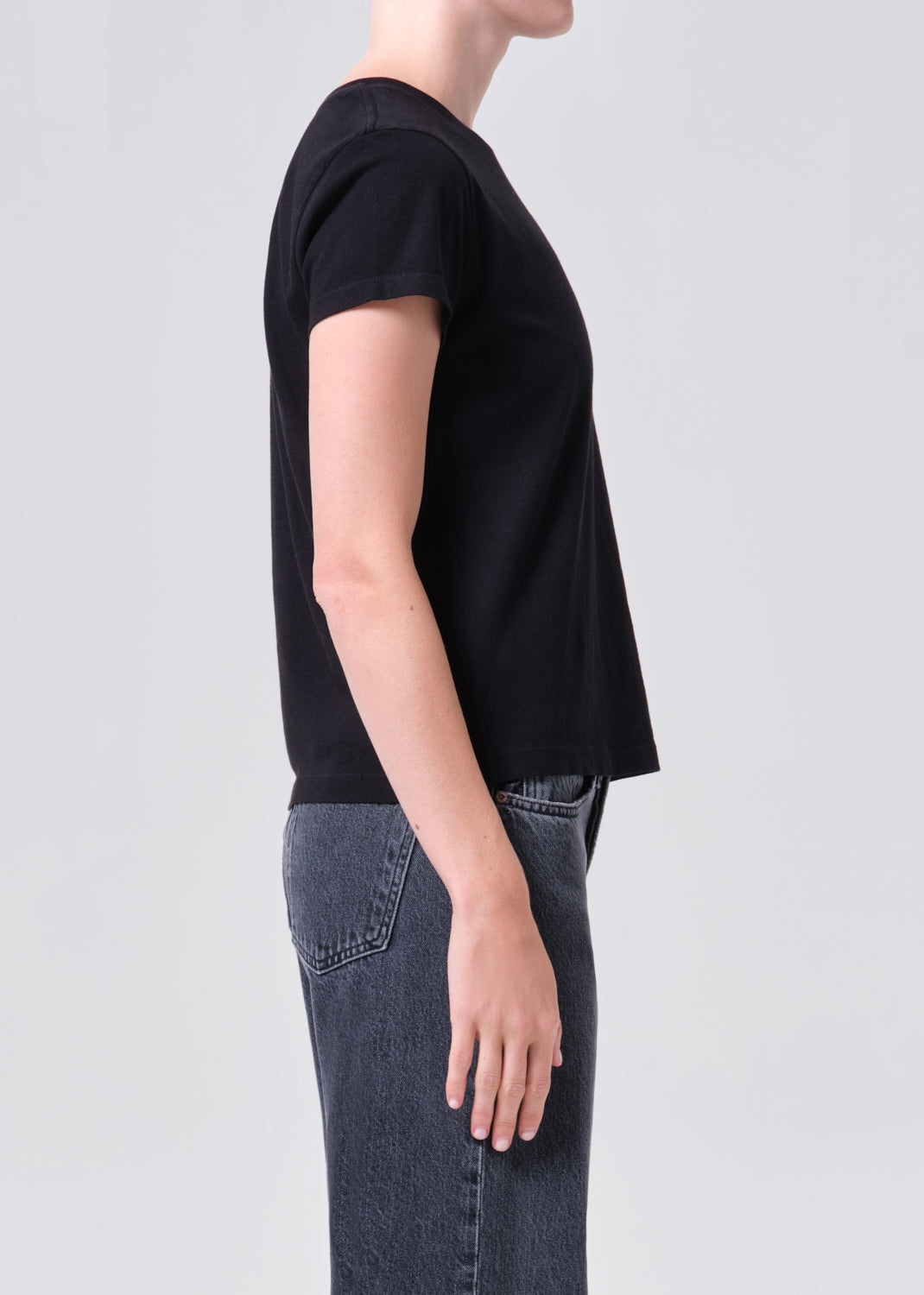 Person wearing a black t-shirt and blue jeans on a light gray background
