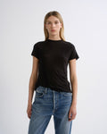 A woman modeling a plain black short-sleeve crewneck t-shirt paired with blue jeans, standing against a light gray studio background.