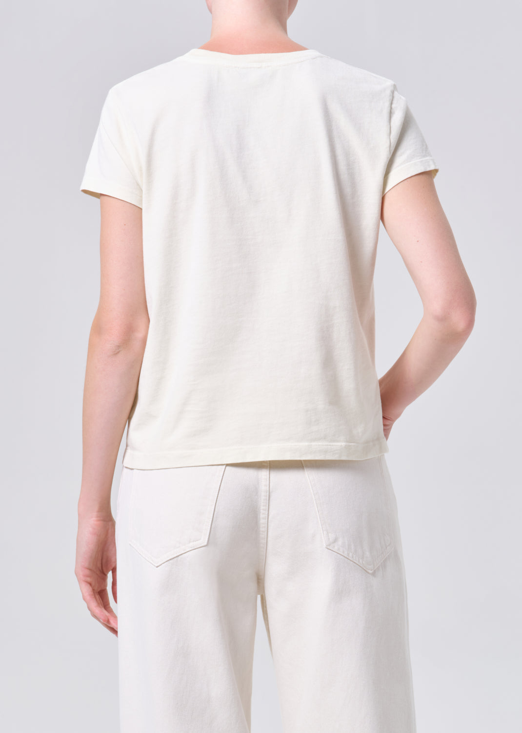 Person wearing a plain white t-shirt and pants on a light gray background