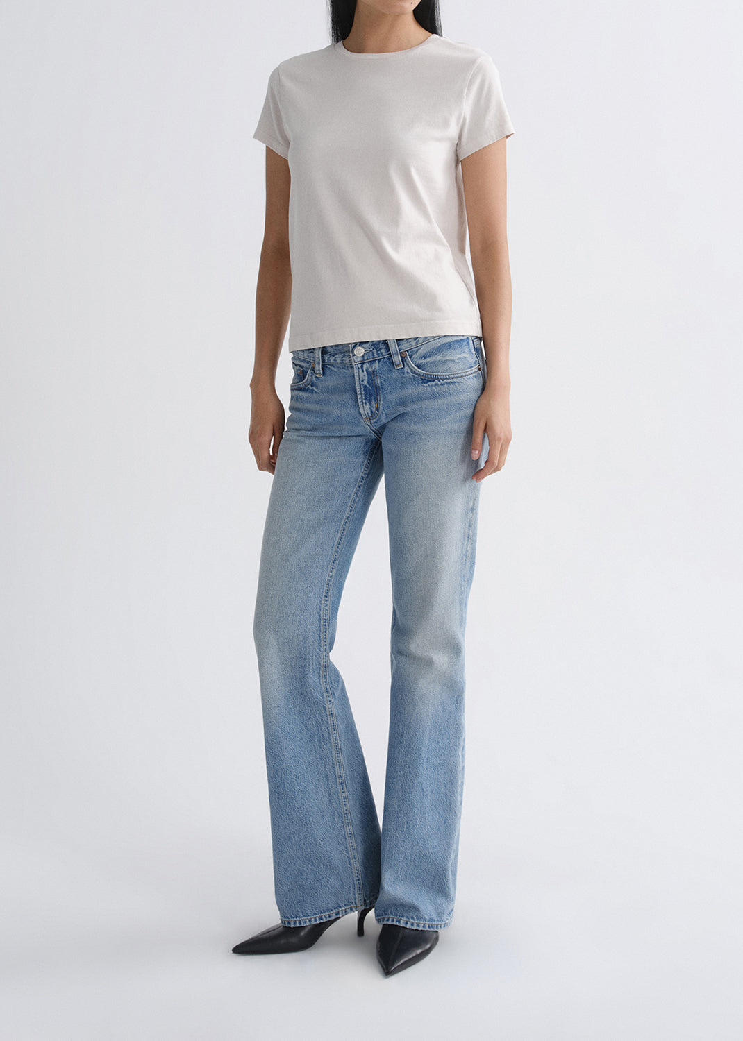 Person wearing light blue jeans and a white t-shirt on a grey background