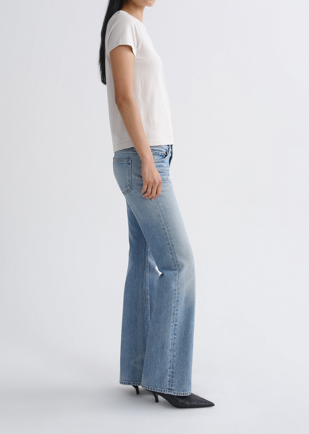 Person wearing light blue jeans and a white top on a grey background