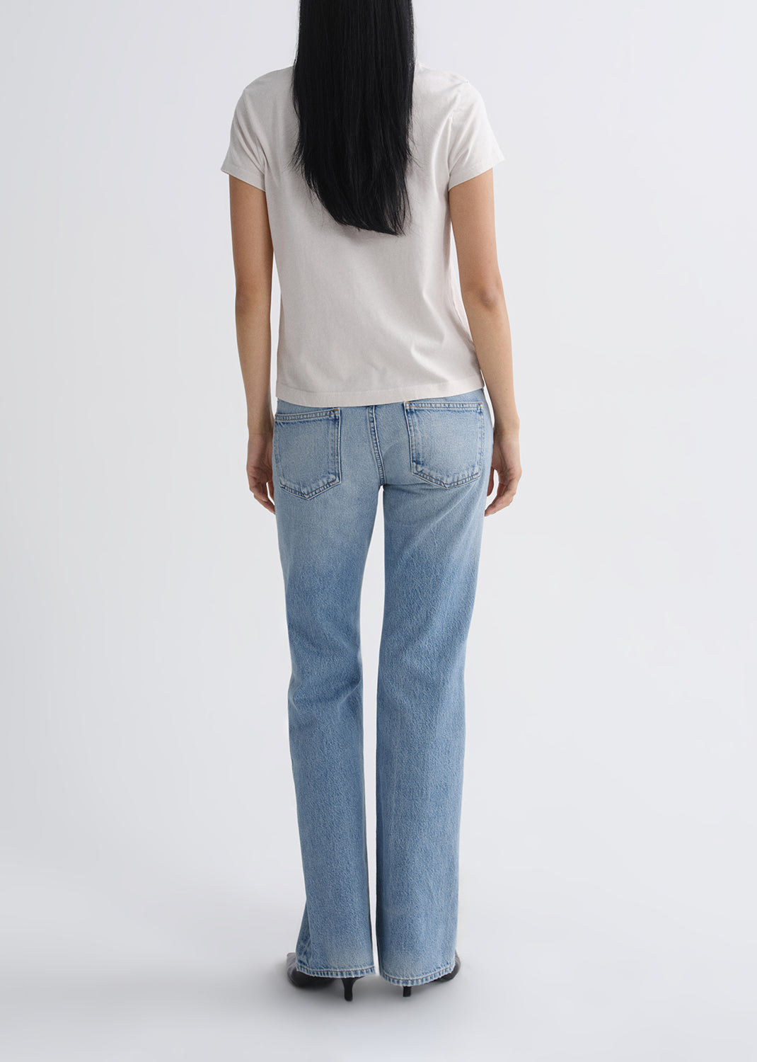 Person wearing a white t-shirt and light blue jeans on a grey background