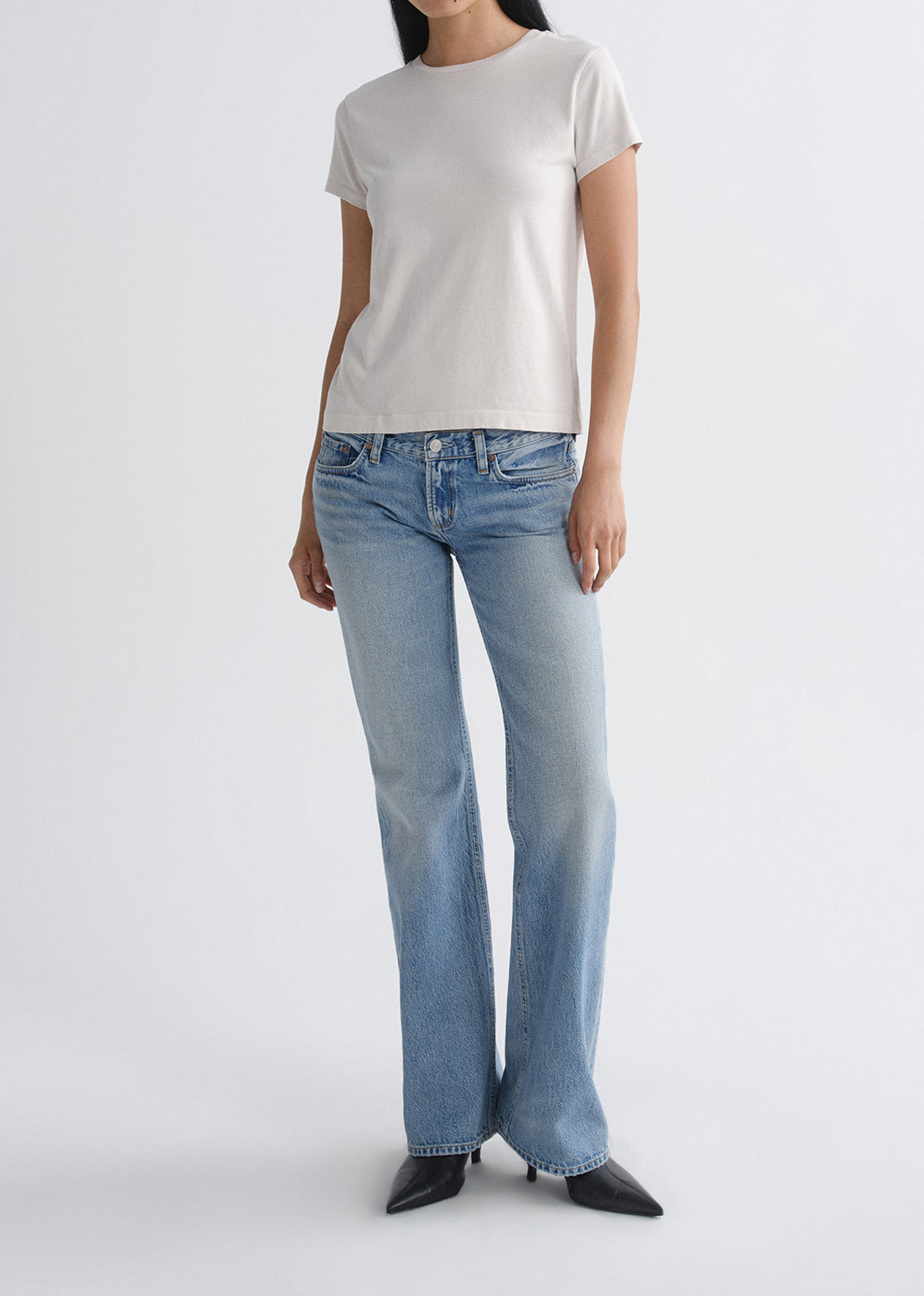 Person wearing a white t-shirt and blue jeans on a grey background