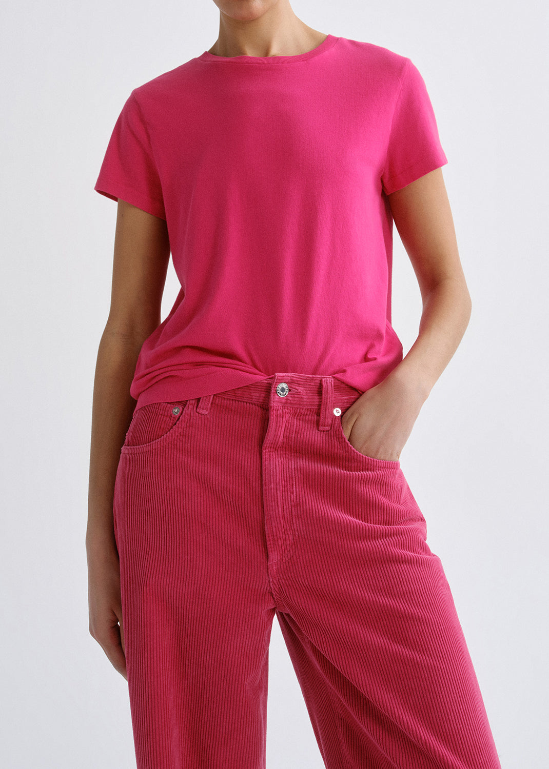 Person wearing a bright pink short sleeve crewneck tee with bright pink straight leg jeans on a grey background