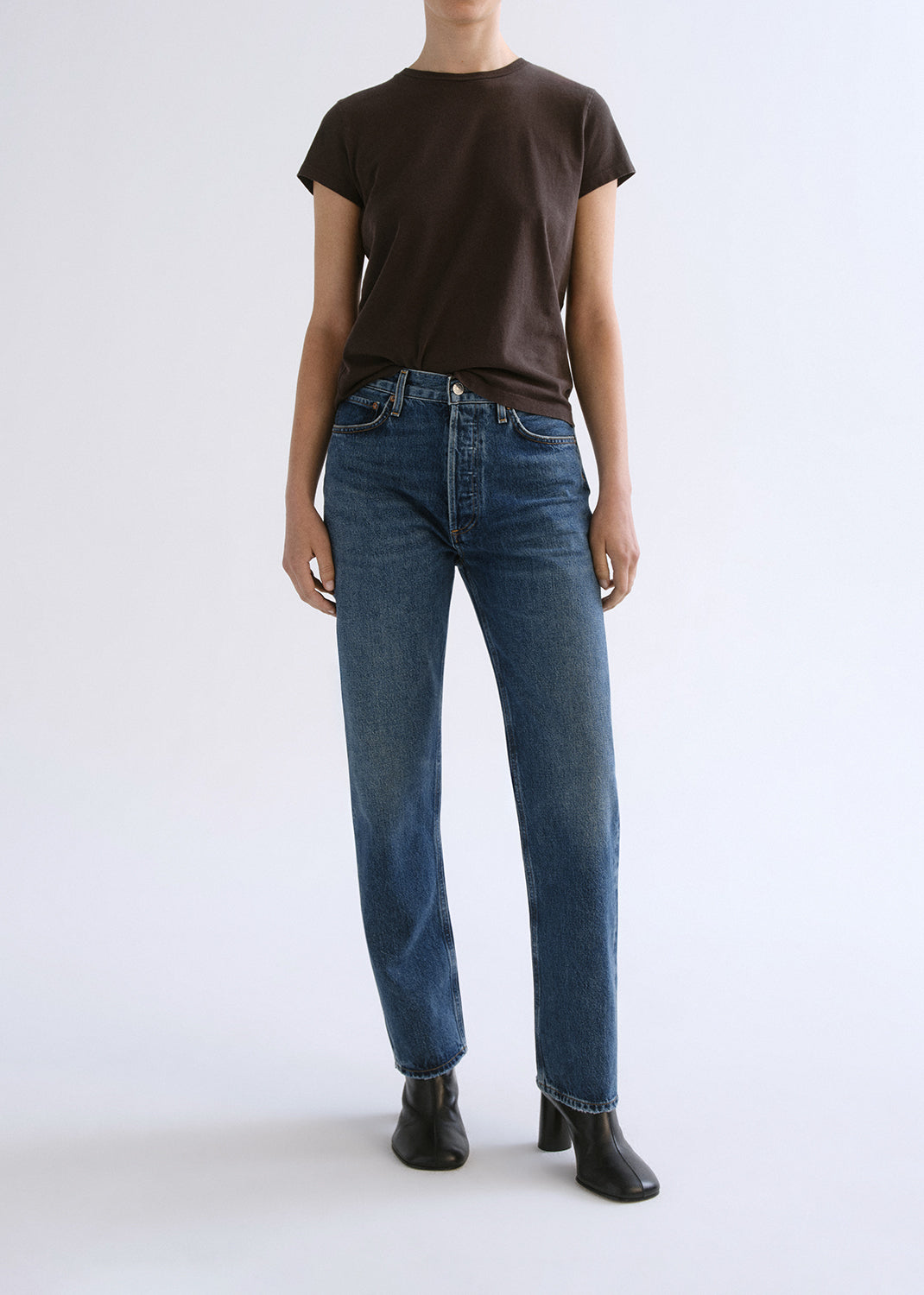 Person wearing a brown shirt and blue pants on a grey background