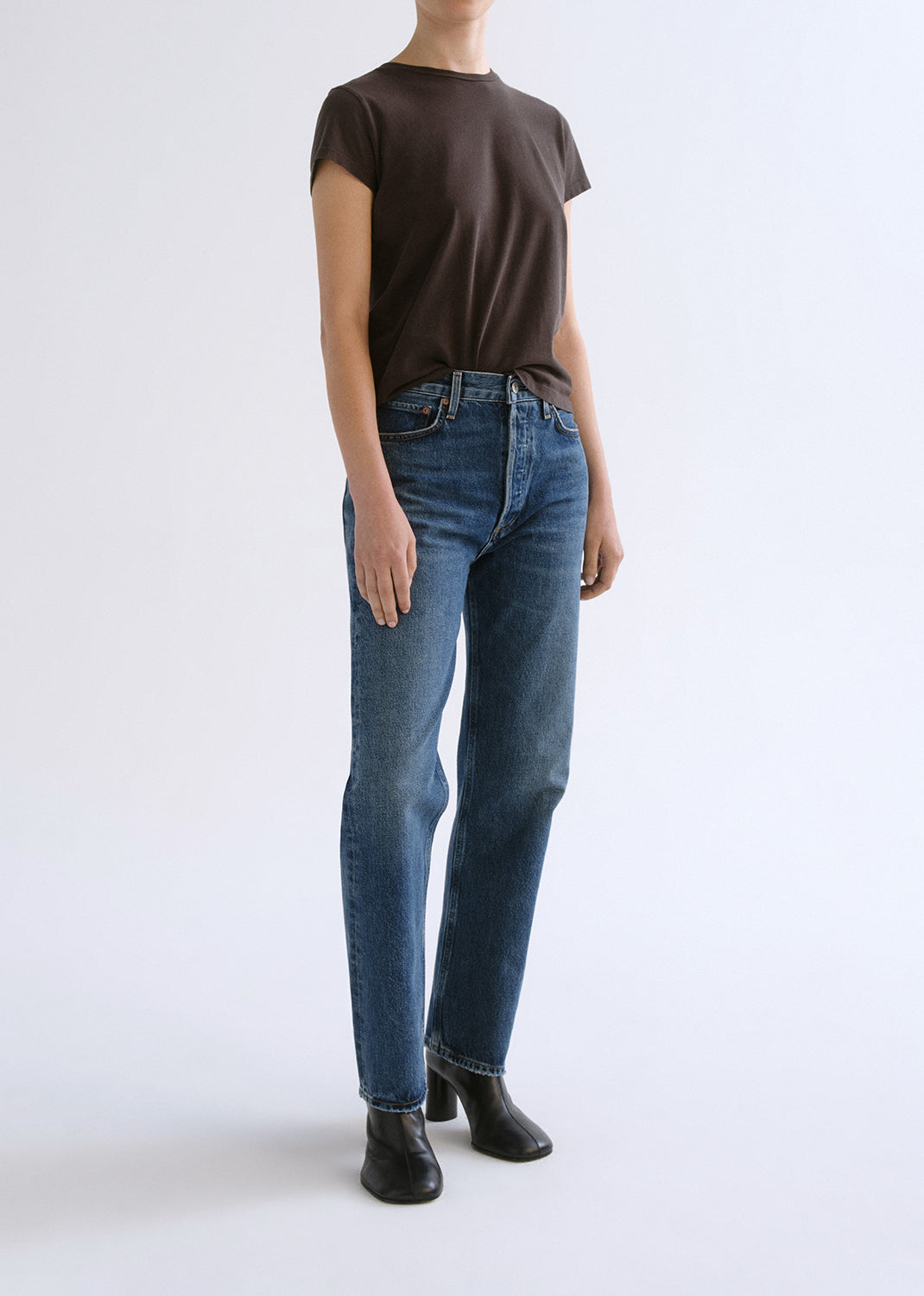Person wearing a brown shirt and blue pants on a grey background