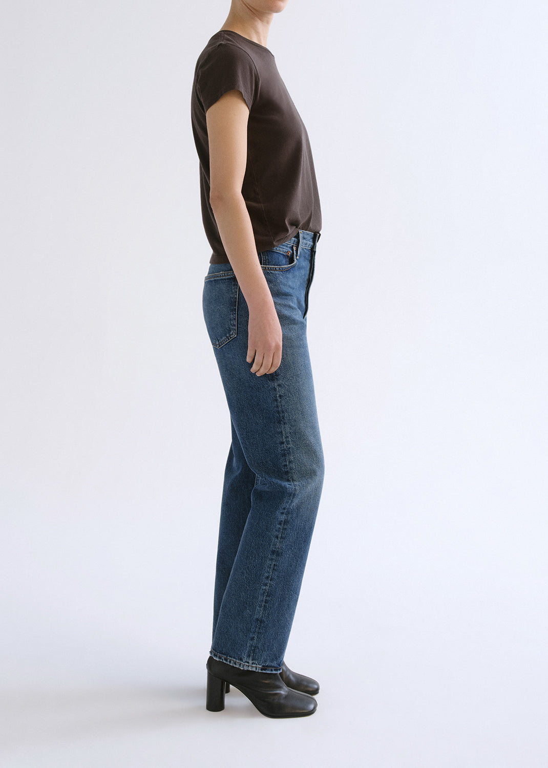 Person wearing a brown shirt and blue pants on a grey background
