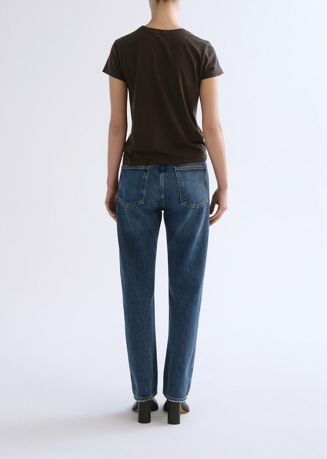 Person wearing a brown shirt and blue pants on a grey background